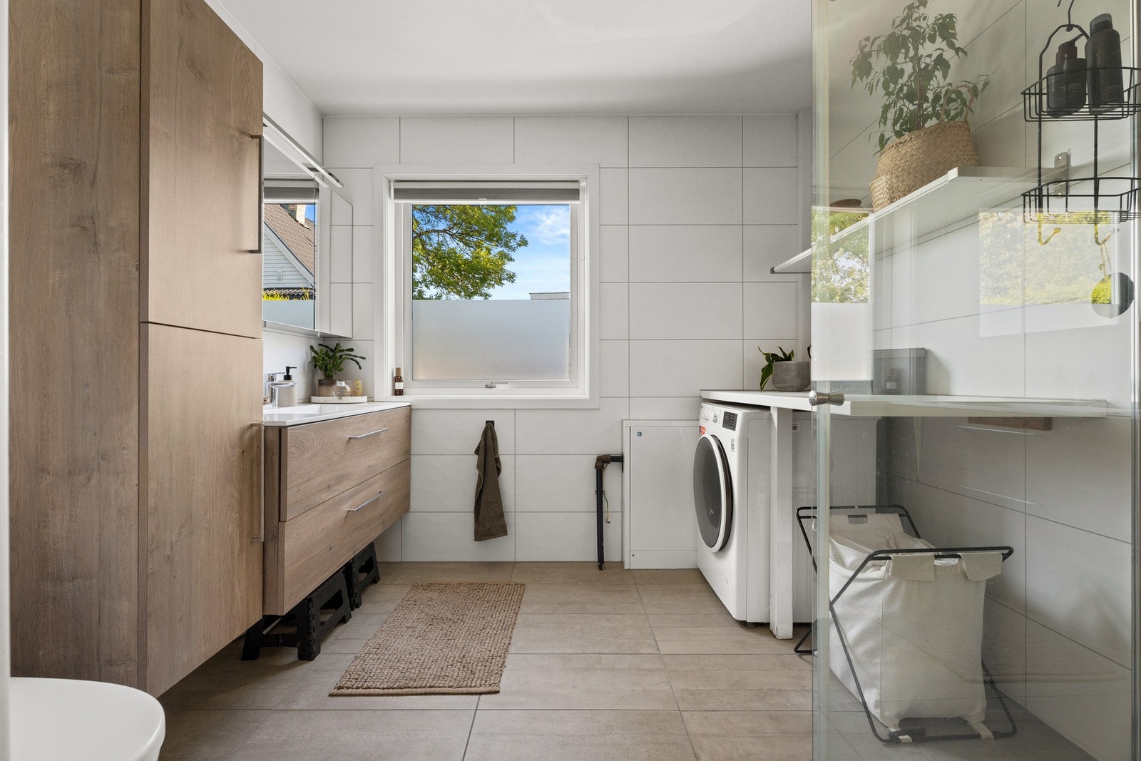 Badet har hvite våtromsplater på veggene og mørkt belegg på gulvet, og av innredning er det en sort skuffeseksjon, heldekkende servant og et stort speil med belysning. Galleribilde