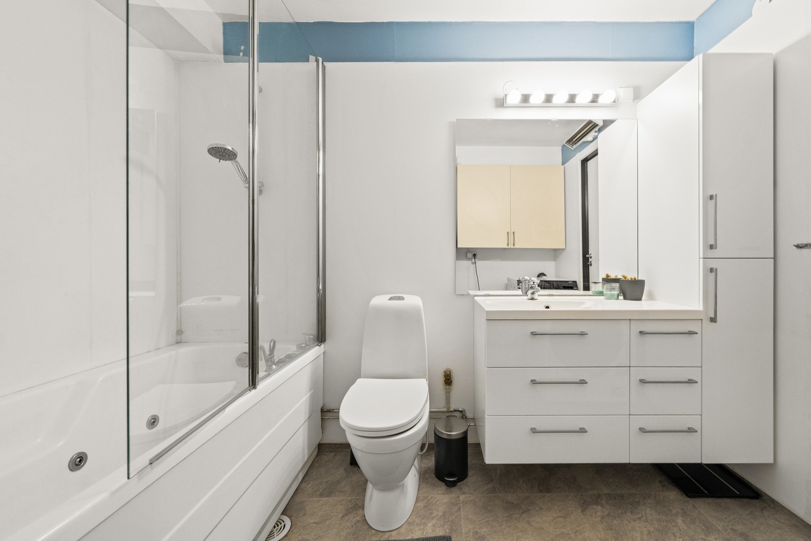 Lyst og romslig bad med moderne innredning, speil med belysning og praktisk badekar med glassfelt. Galleribilde