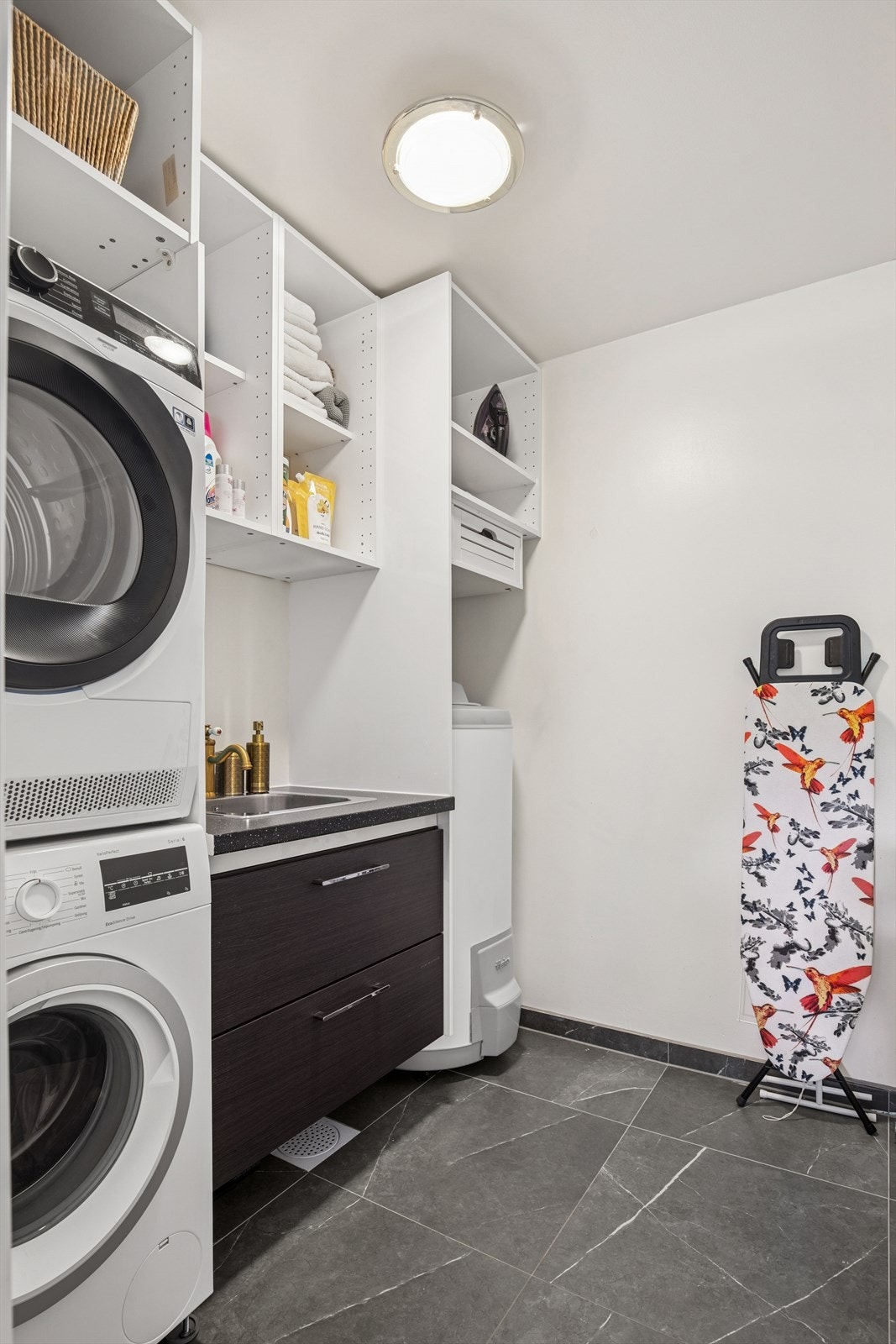 Praktisk og velutstyrt vaskerom fra 2020 med flislagte flater, sort innredning med nedfelt servant. Rommet har opplegg for vaskemaskin og plass til tørketrommel, samt varmtvannsbereder. Det er montert plastsluk. Galleribilde