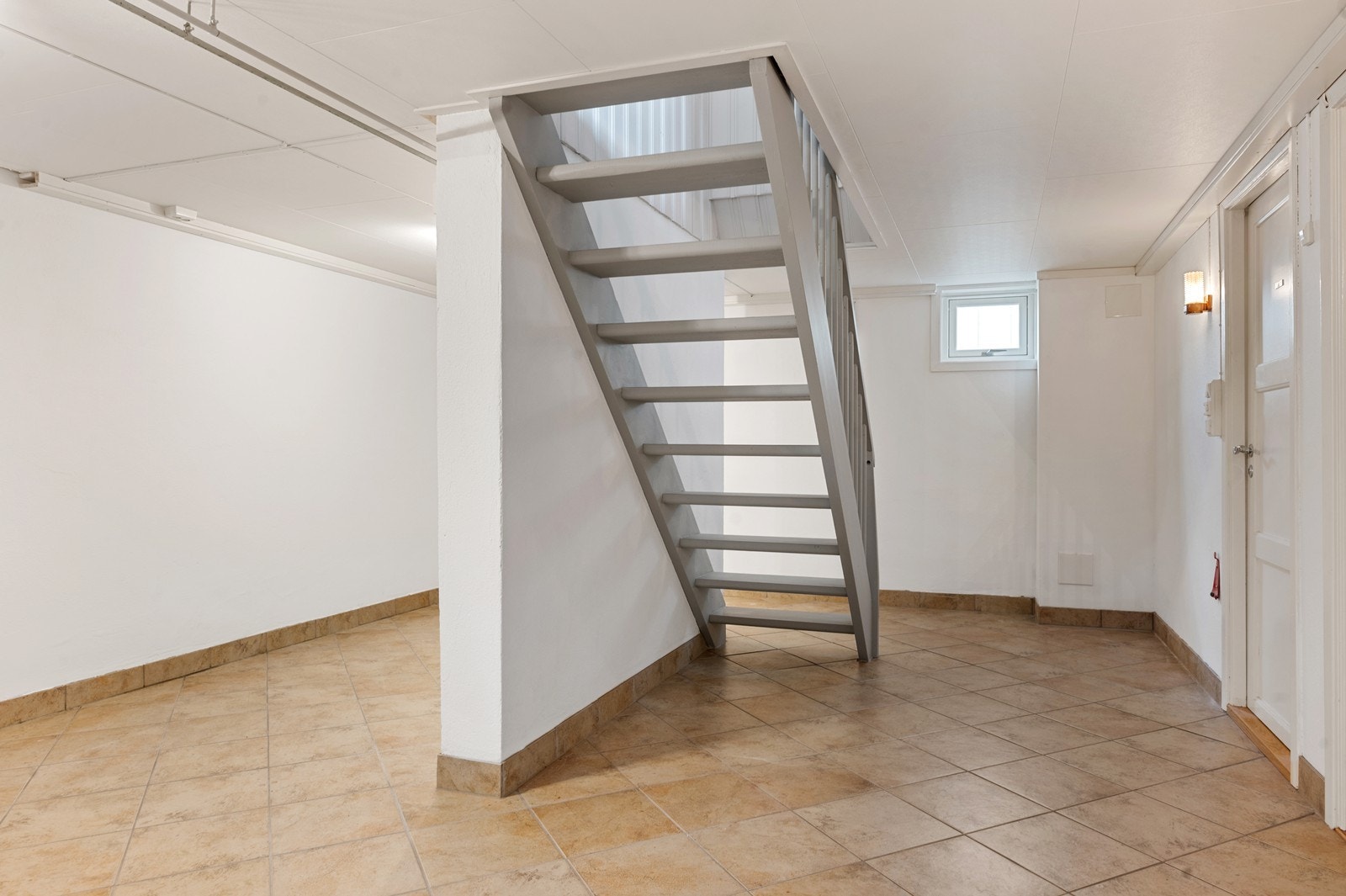 Trapperommet i kjelleren har flislagt gulv og leder videre til flere praktiske rom. Her er det godt med lagringsplass. Galleribilde