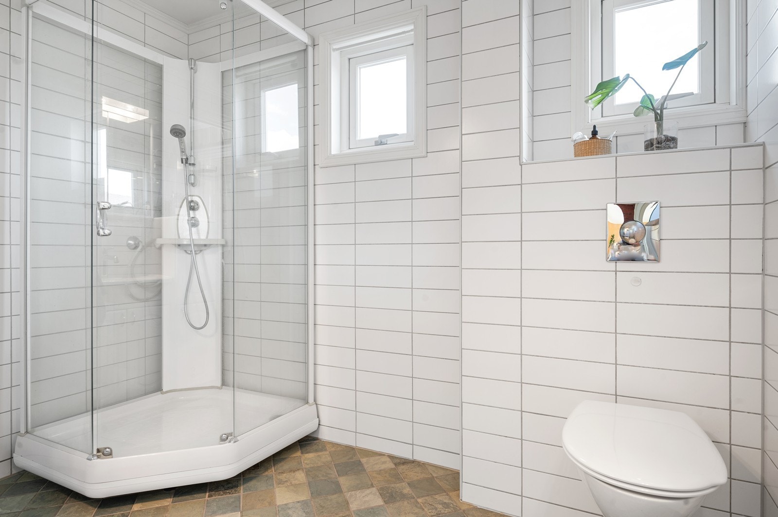 Delikat, flislagt bad fra 2006 innredet med vegghengt toalett og dusjkabinett. Galleribilde