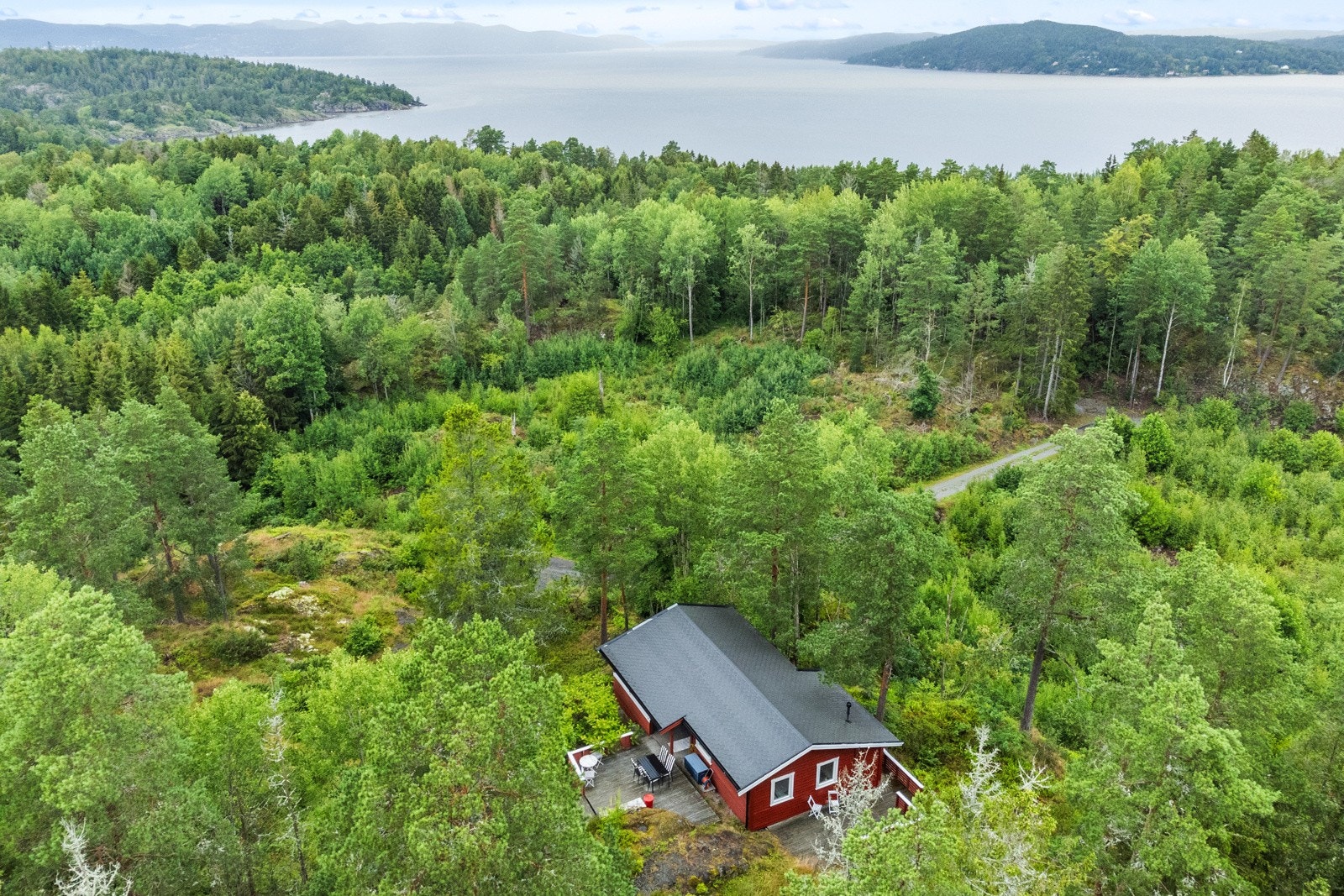 Hytta ligger høyt og tilbaketrukket fra veien med utsikt over trekronene og fjell i horisonten. Galleribilde