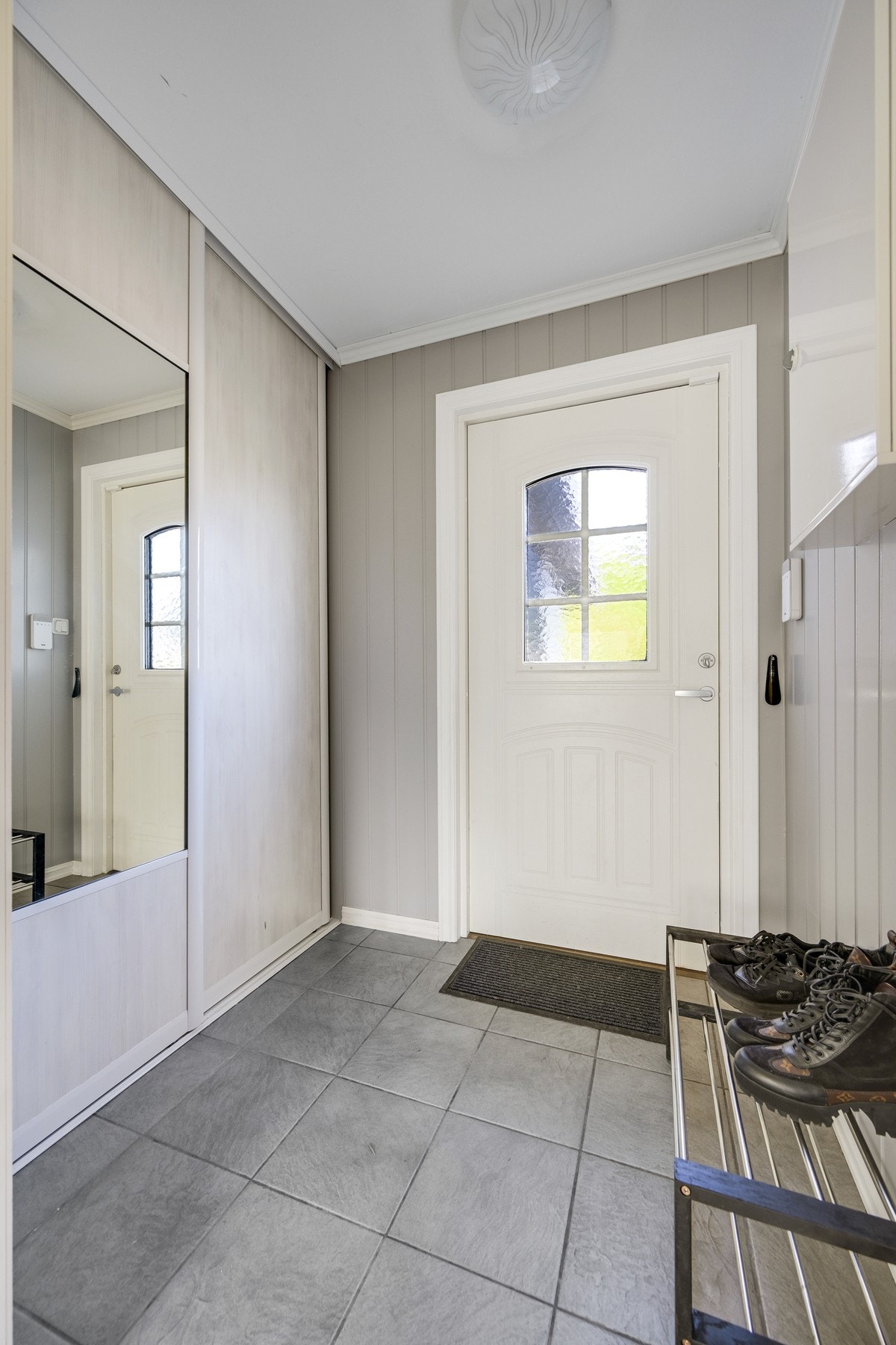 Lys og innbydende entré med flis på gulvet og malte vegger. Her er det praktisk skyvedørsgarderobe for enkel oppbevaring av klær og sko. Galleribilde