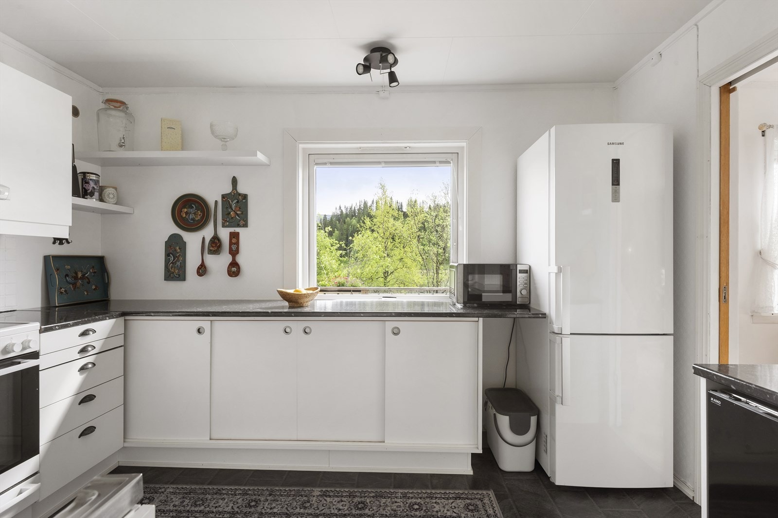 Romslig kjøkken innredet med slette fronter, laminert benkeplate og frittstående hvitevarer. Galleribilde