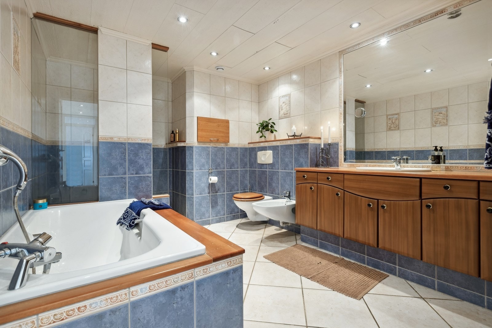 Baderommet er innredet med servantinnredning, innfliset badekar, veggfestet klosett med innebygget sisterne og dusj på gulv. Galleribilde