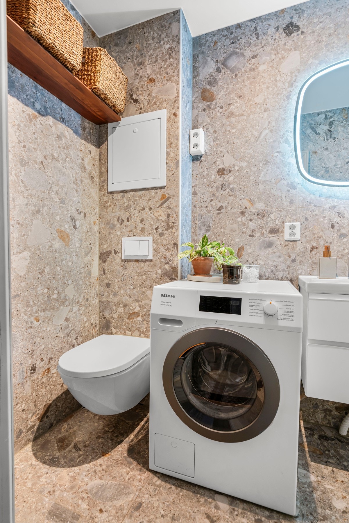 Plassbesparende vegghengt toalett, opplegg for vaskemaskin og lekkert servantskap med sminkespeil med innebygd lys. Galleribilde