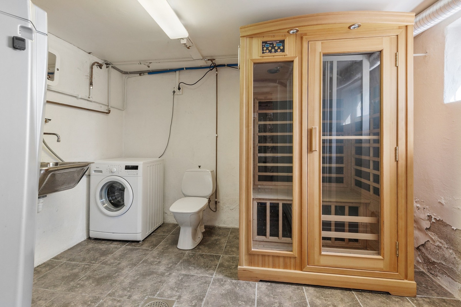 Vaskerom innredet med gulvmontert toalett, utslagsvask i stål, opplegg for vaskemaskin og dusjkabinett Galleribilde