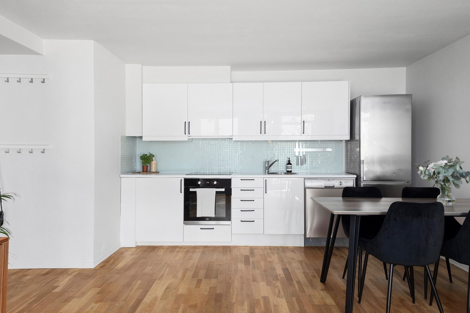 Kjøkkeninnredningen er stilren med hvite, matte fronter og laminert benkeplate med fliser over, som gir et pent og helhetlig uttrykk. Galleribilde