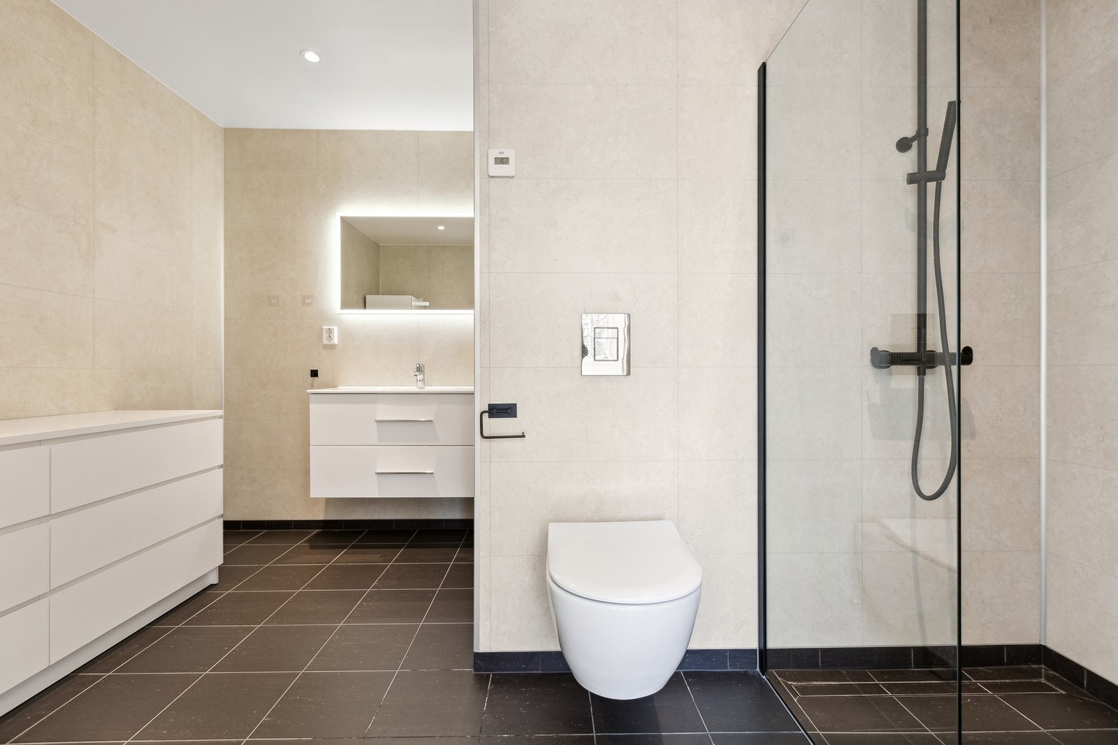 Badet er utstyrt med heldekkende servant, vegghengt toalett og dusjhjørne med glassvegg - stilrent og funksjonelt Galleribilde