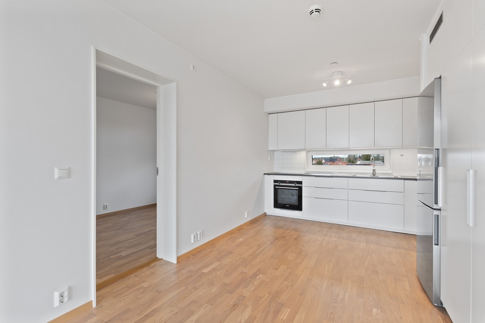 Stilrent kjøkken fra Ikea, nytt i 2020. Innredningen består av hvite slette fronter med foring opp til tak og laminert benkeplate med nedfelt vaskekum i rustfritt stål. Galleribilde