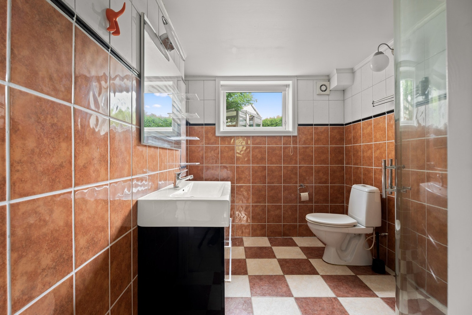 Baderom fra 2009 med fliser på gulv og vegger. Inventar består av servantinnredning, gulvmontert toalett, opplegg og plass til vaskemaskin, samt dusj med glassdører Galleribilde