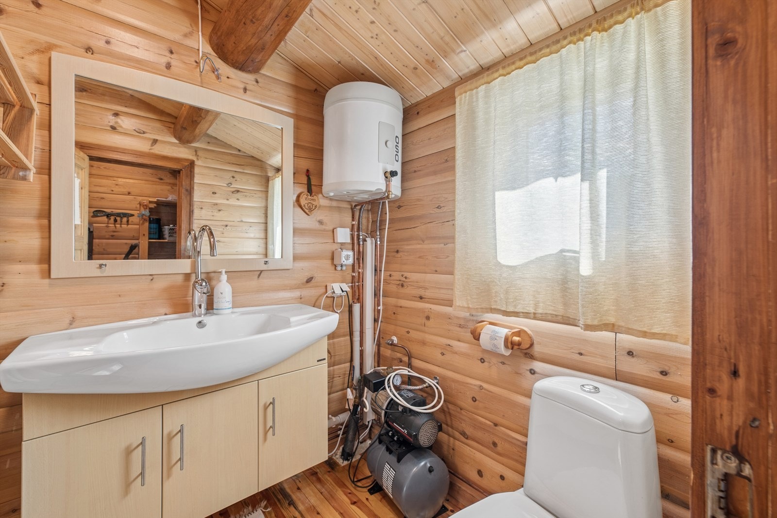 Toalettrommet har et rustikt og innbydende uttrykk med furugulv, tømmervegger og panel i himlingen, som gir en varm og tradisjonell atmosfære. Galleribilde