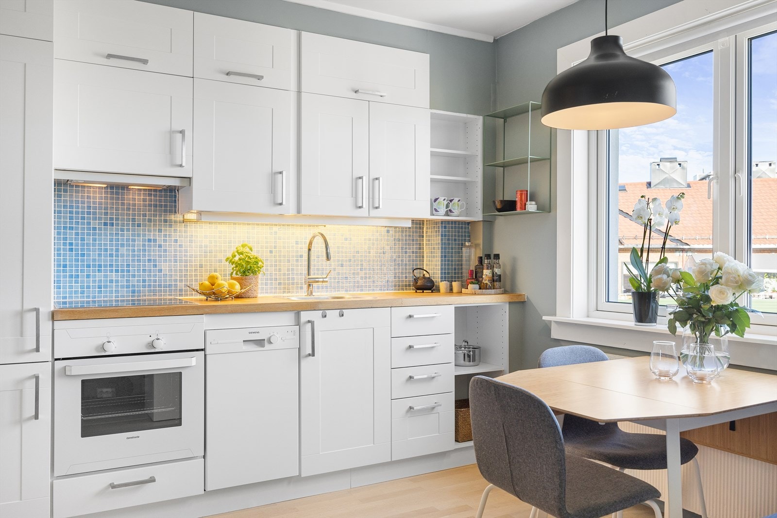 Moderne kjøkkeninnredning med hvite profilerte fronter, benkeplate i tre og fliser mellom overskap. Galleribilde