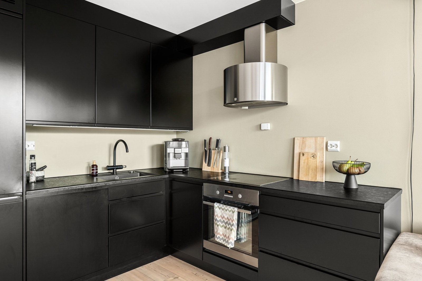 Kjøkkeninnredning med mekanisk avtrekksvifte over stekesonen. Det er integrert platetopp, stekovn, oppvaskmaskin og kjøl-/fryseskap. Galleribilde