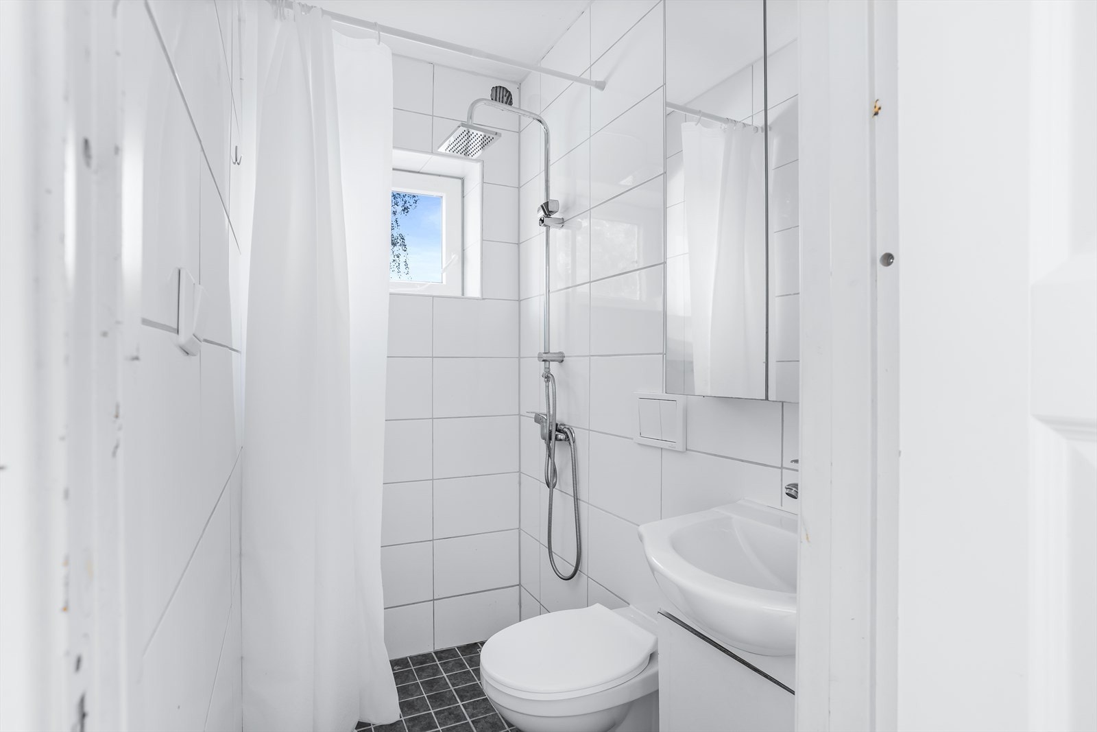 Badet er innredet med servantskap med en overliggende servant, speilskap, vegghengt toalett og dusjhjørne med forheng. Galleribilde