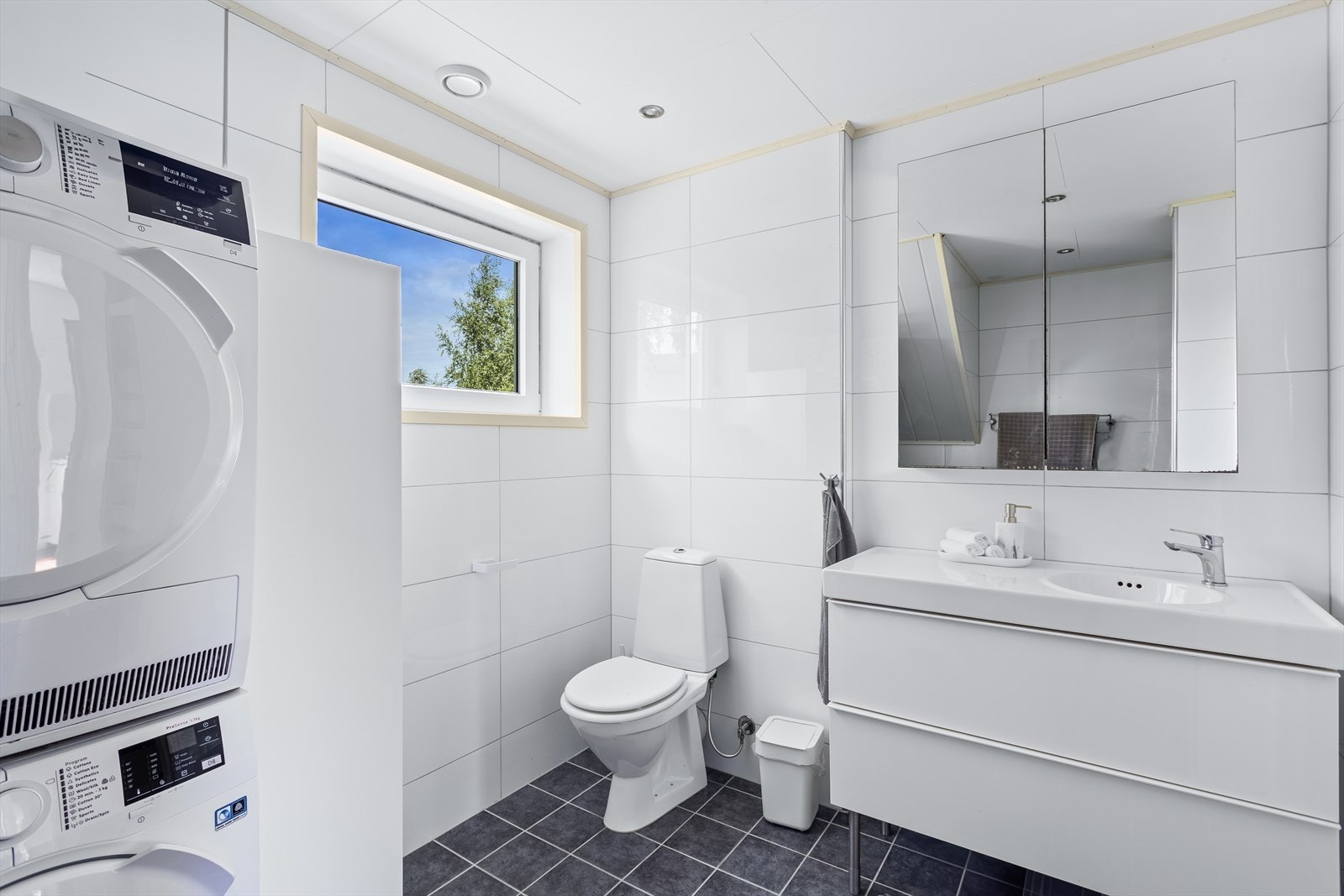 Badet er innredet med servantskap, speil, toalett, dusjhjørne og opplegg for vaskemaskin. Galleribilde