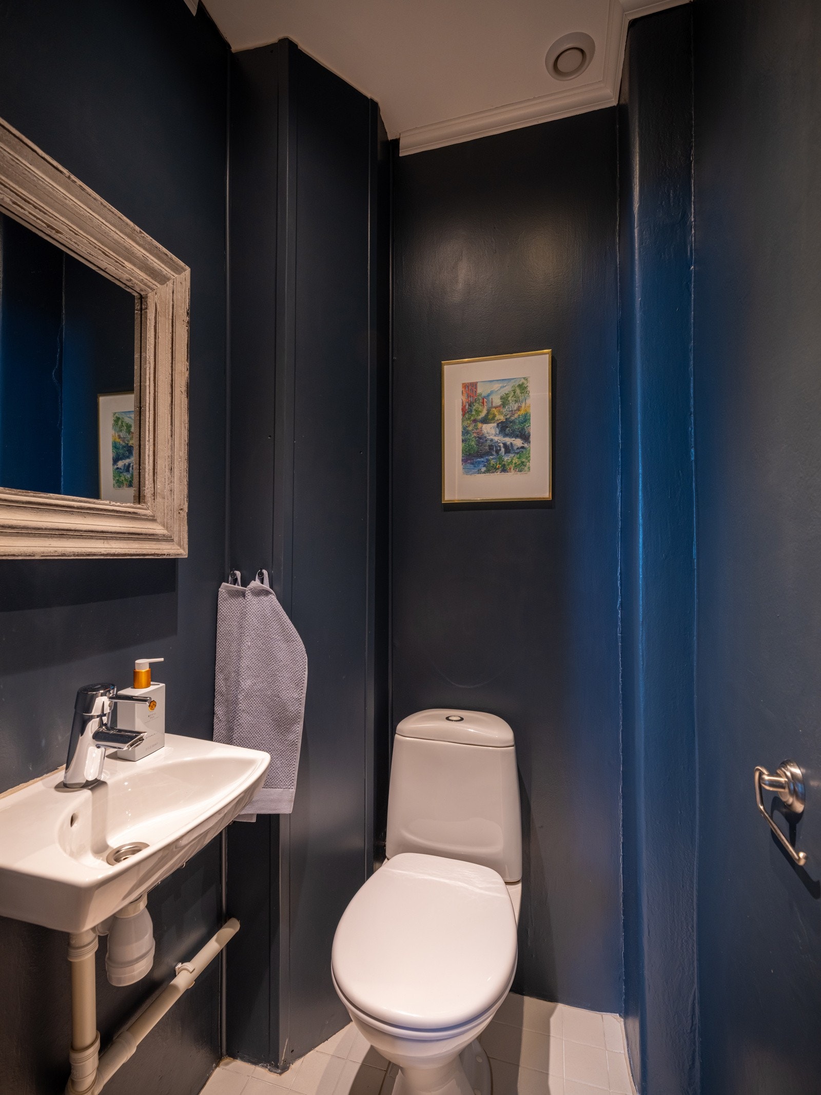 Leiligheten har et praktisk toalettrom med servant, gulvstående toalett og fliser på gulvet. Galleribilde