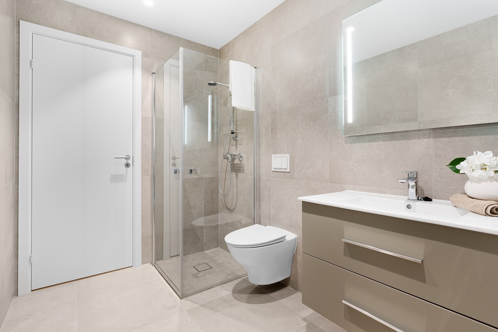 Flott flislagt bad med vegghengt toalett, servant med innredning og dusjhjørne Galleribilde