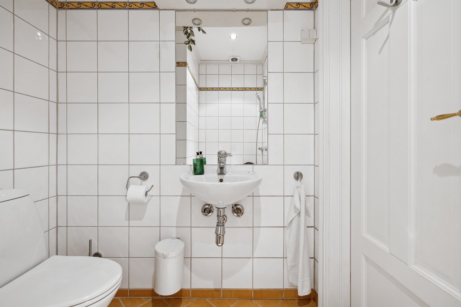 Flislagt baderom utstyrt med gulvmontert wc, servant med ett-greps blandebatteri, speil og belysning Galleribilde