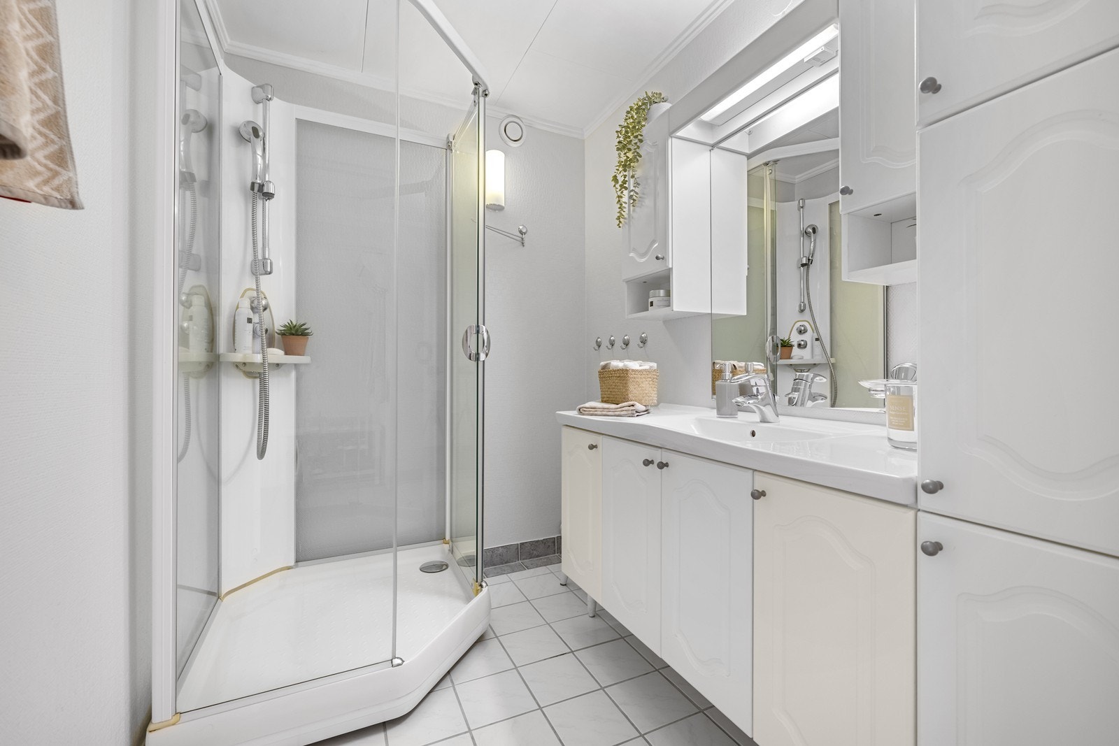 Bad med flis på gulv og malte vegger, hvite plater i tak. Det er varmekabler i gulv og avtrekk til felles ventilasjon. Badet har sanitærutstyr som dusjkabinett og vask. Galleribilde