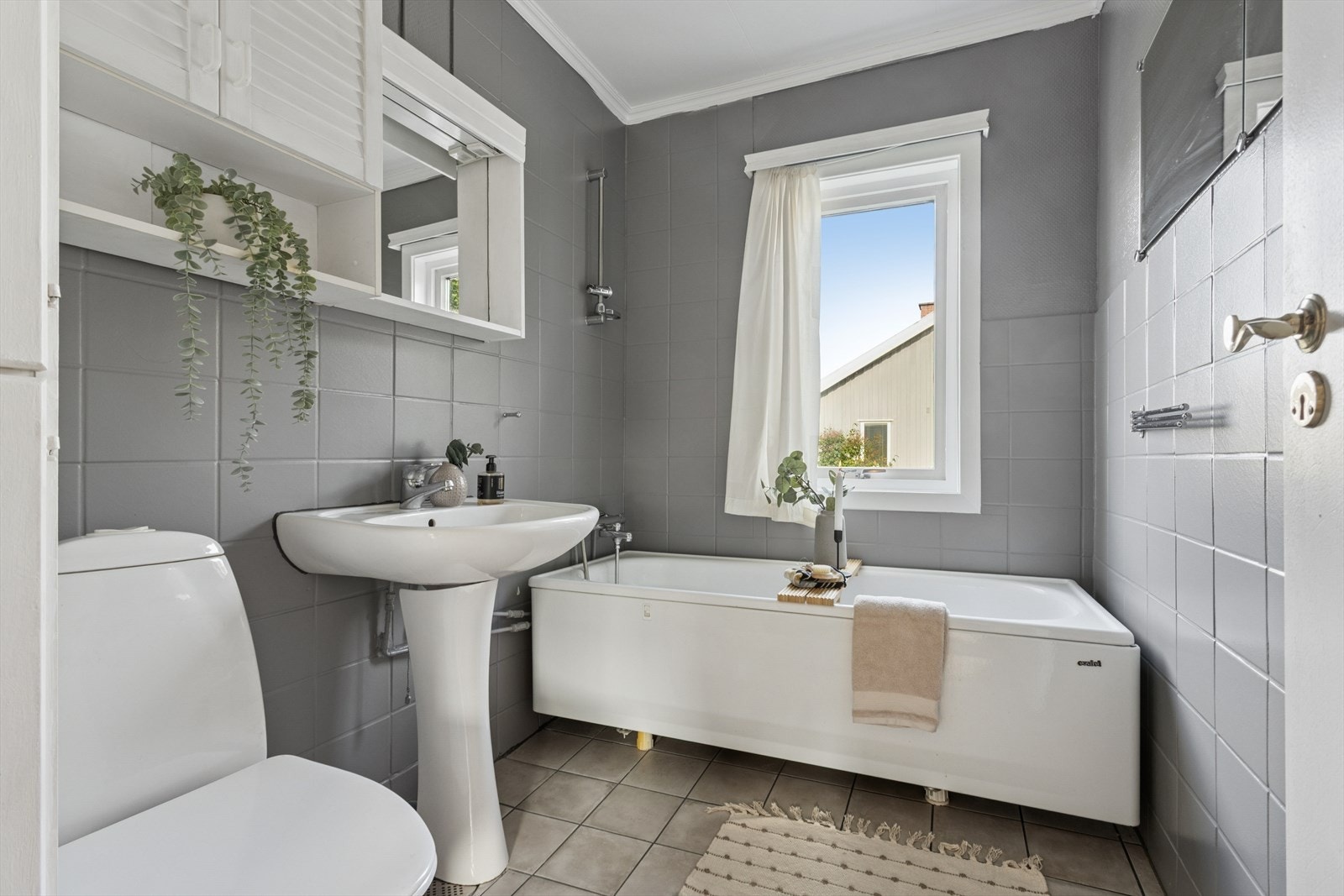 Flislagt baderom med varmekabler i gulv, utstyrt med søyleservant, badekar og toalett. Galleribilde