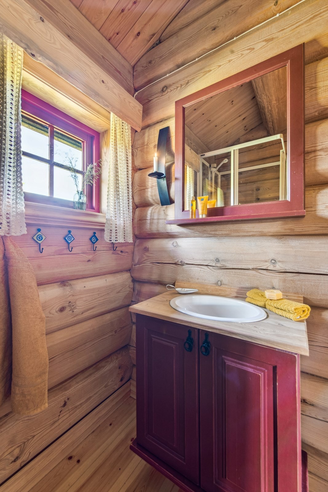 Et enkelt og funksjonelt sanitærrom med lakkert furugulv, ubehandlede laftevegger og panel i himlingen. Rommet er utstyrt med dusjkabinett, baderomsinnredning og servant. Galleribilde