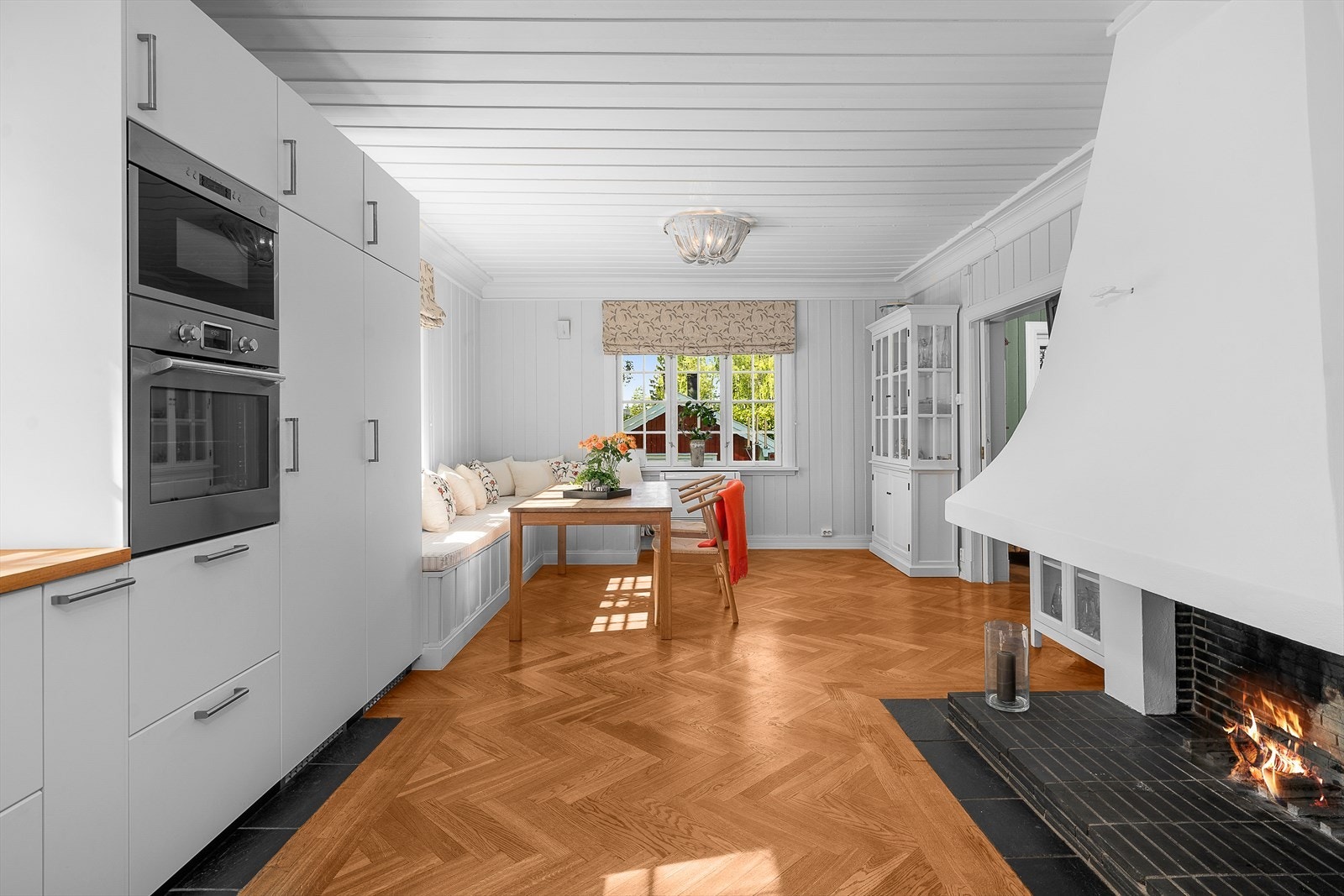 Kjøkken med stor åpen peis på gulvnivå og spisekrok/ allrom på enden Galleribilde