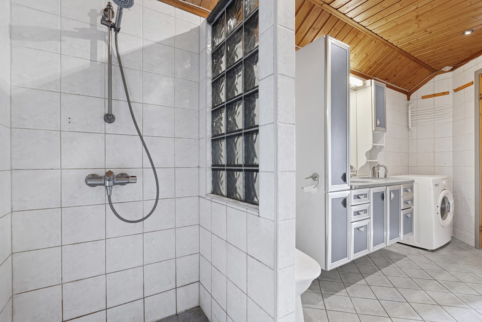 Badet er utstyrt med blant annet romslig dusjhjørne, opplegg for vaskemaskin, downlights i tak, toalett og servant med oppbevaring. Galleribilde