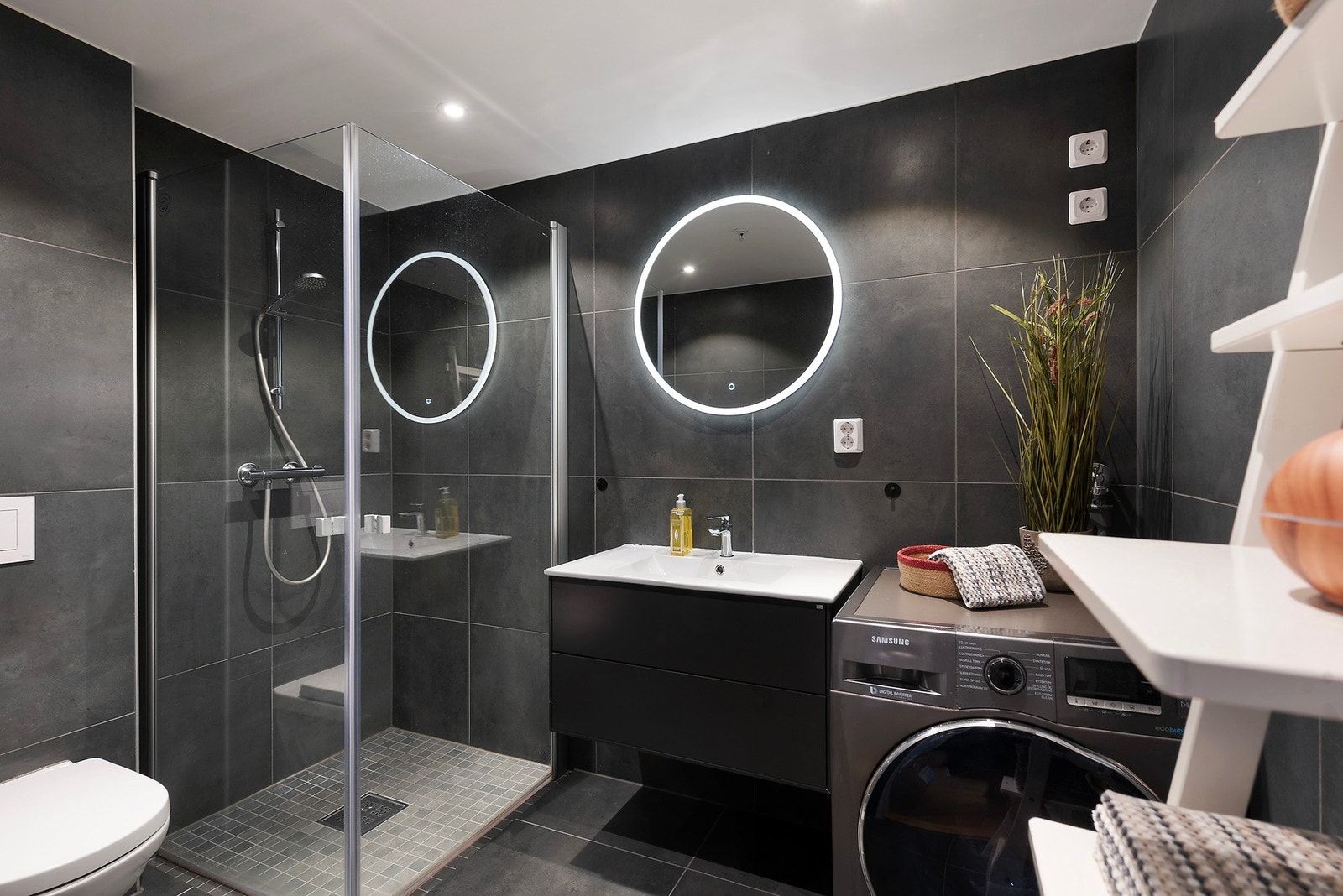 Badet er lekkert og moderne utført med mørke fliser på gulv og vegger, hvitmalt himling med downlights og varmekabler i gulvet Galleribilde