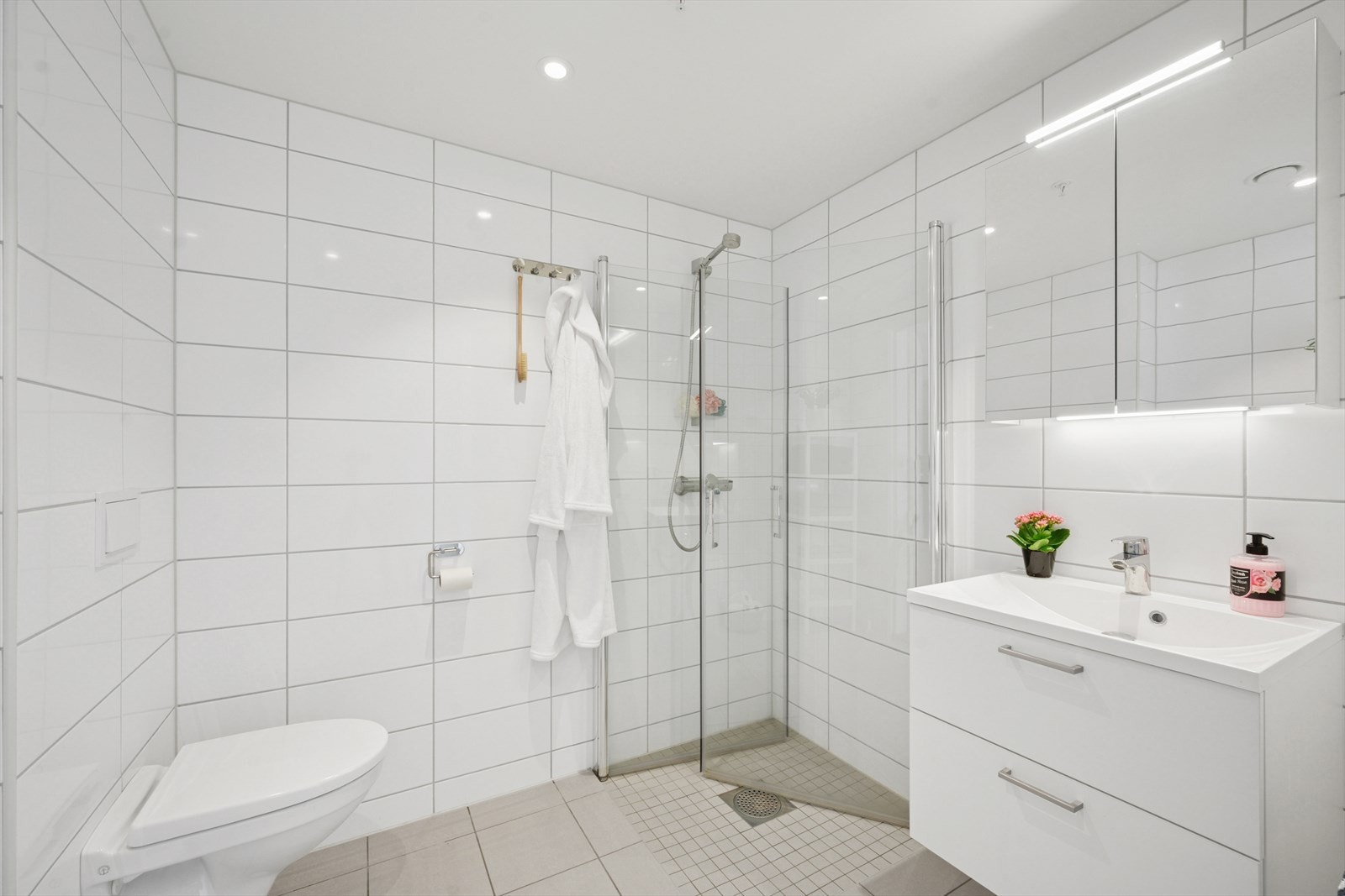 Det andre badet er et delikat baderom som er innredet med dusjhjørne med dusjvegger, servant over innredning med skuffer, speilskap og vegghengt toalett. Galleribilde