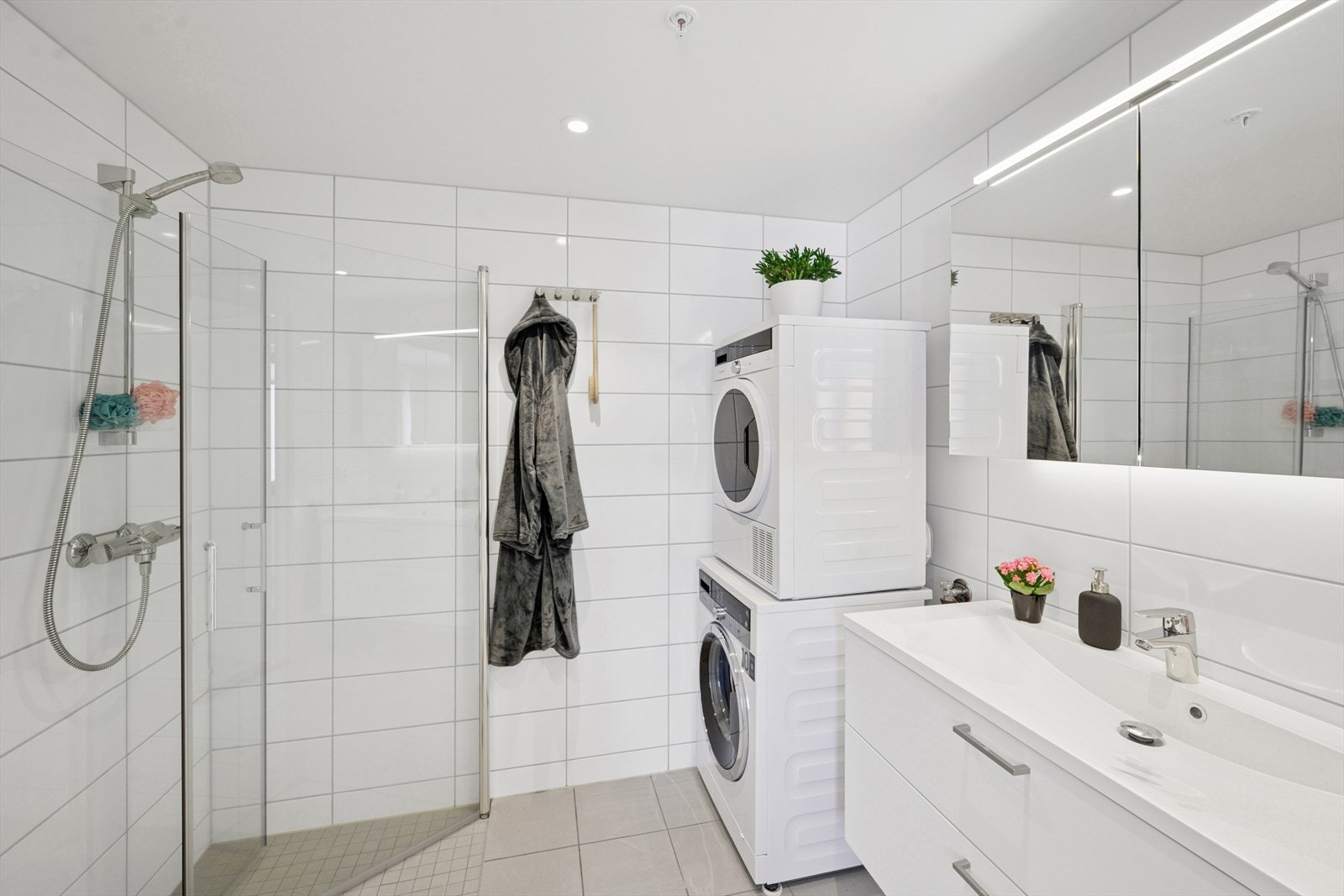 Baderommet har dusjhjørne, servant over innredning med skuffer, speilskap, vegghengt toalett, samt opplegg for vaskemaskin og tørketrommel. Galleribilde