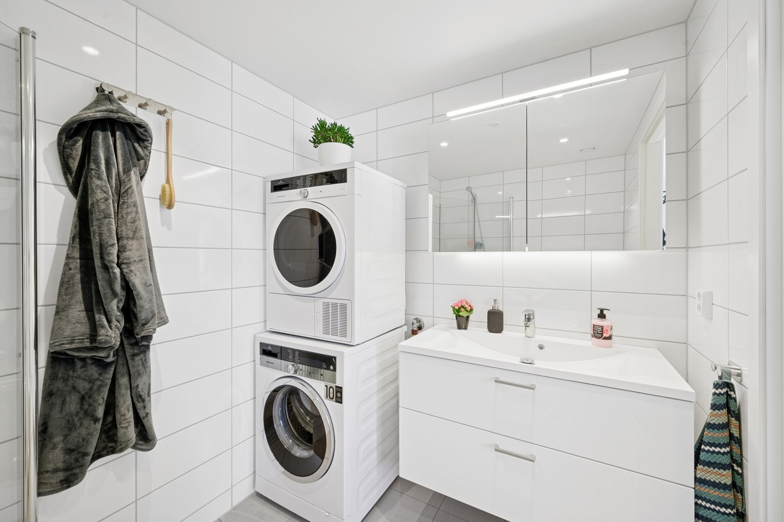 Baderommet har dusjhjørne, servant over innredning med skuffer, speilskap, vegghengt toalett, samt opplegg for vaskemaskin og tørketrommel. Galleribilde