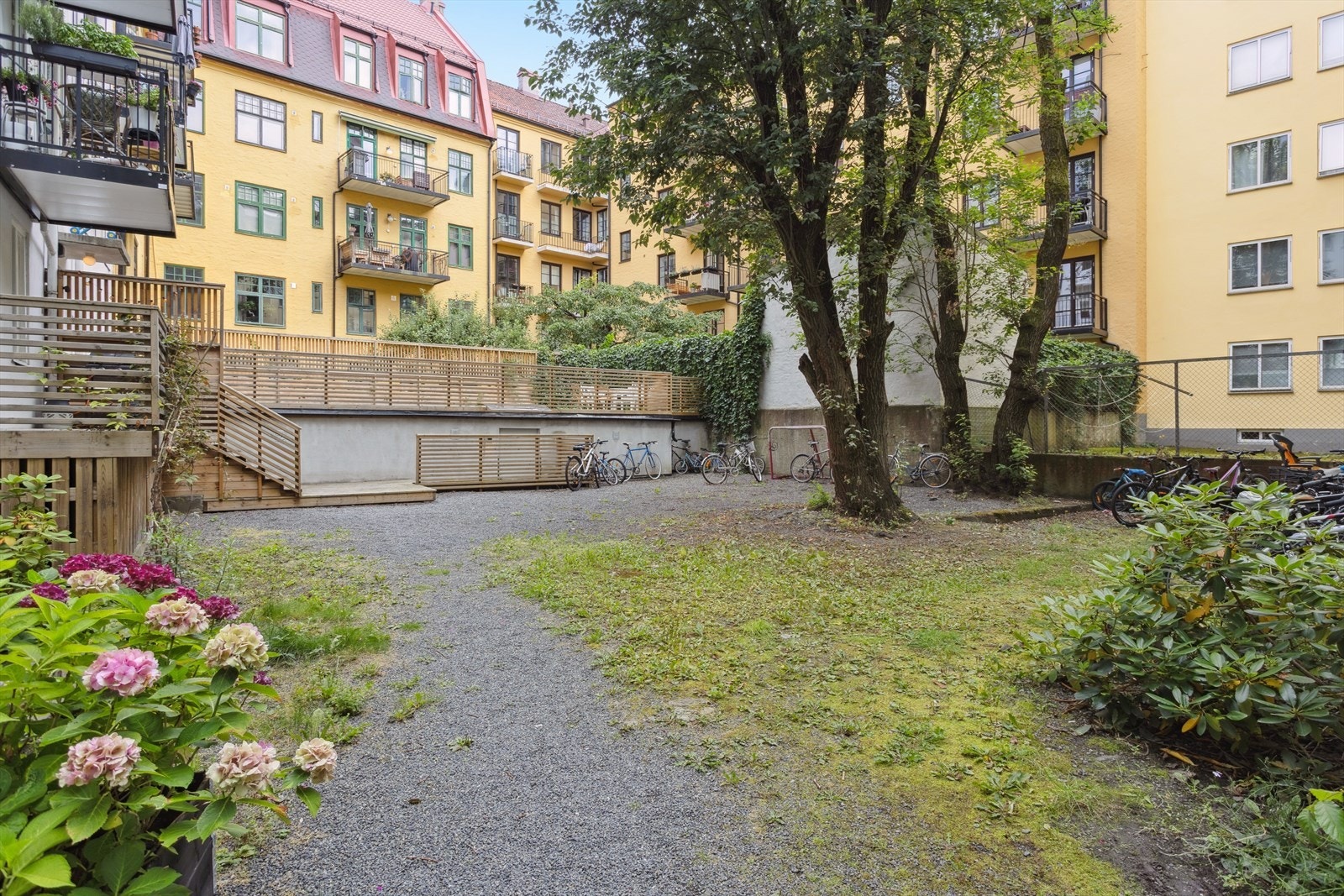 Bakgården er anlagt med grus, trær og variert beplantning, som gir et hyggelig uteområde for beboerne i sameiet. Galleribilde
