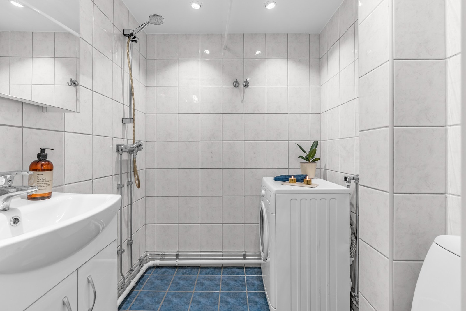 Badet er flislagt med varmekabler i gulvet og måler en takhøyde på ca. 2,19 meter. Innredningen inkluderer et servantskap med speilskap over, samt gulvmontert toalett. Galleribilde