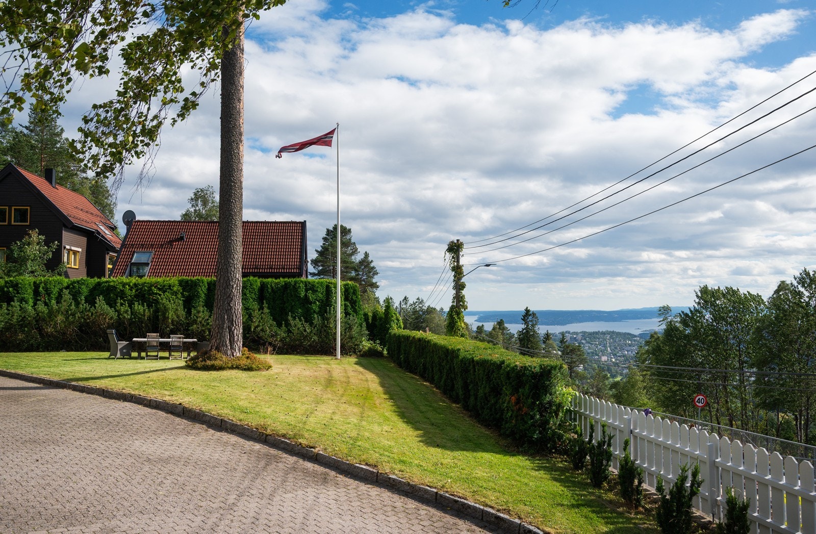 Eiendommen ligger godt tilbaketrukket og høyt hevet over veien skjermet med både gjerde og vintergrønn hekk Galleribilde