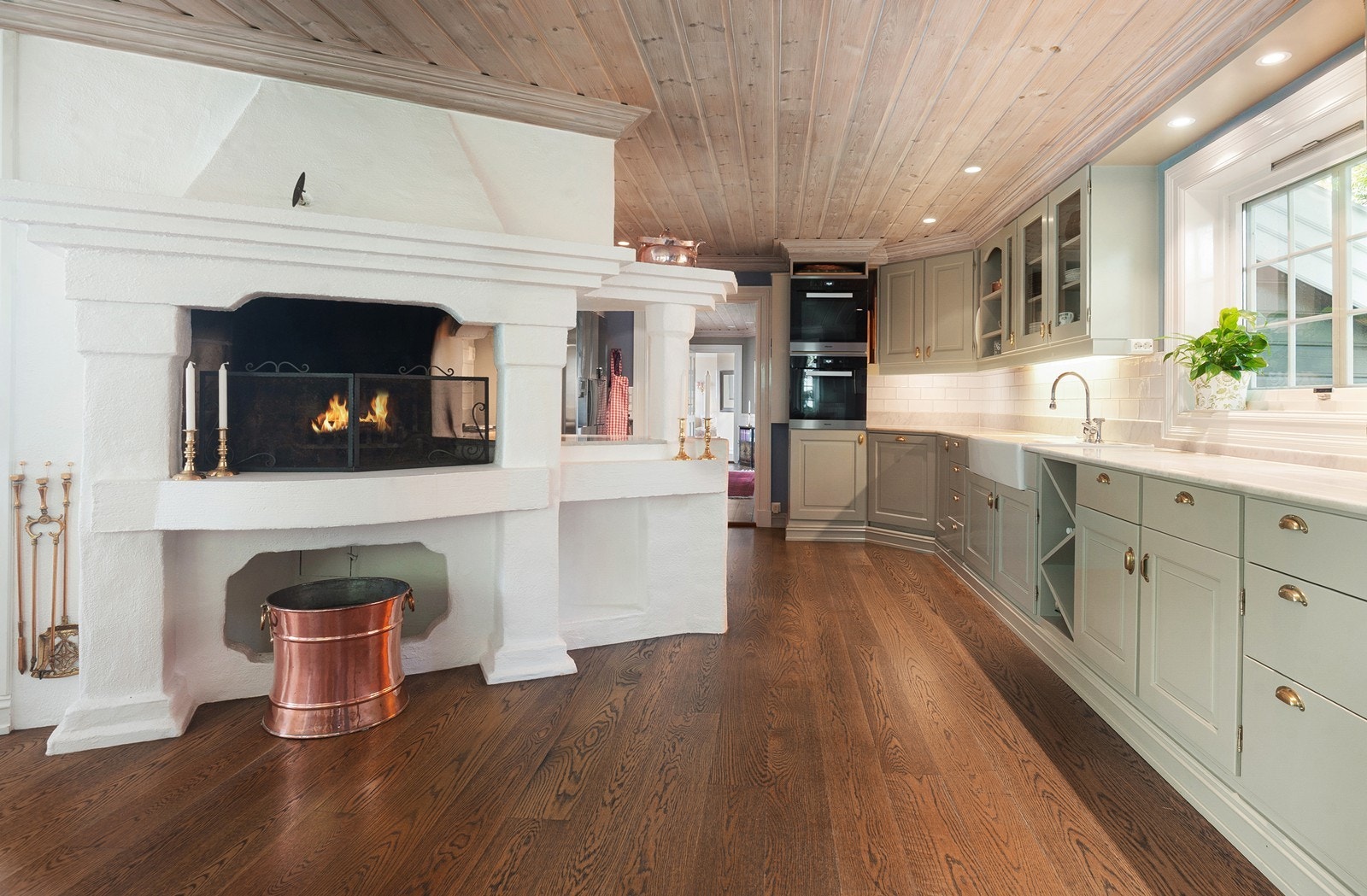Koselig peis i sittehøyde og klassisk solid kjøkkeninnredning innover rommet gjennomgående mot trappehallen Galleribilde