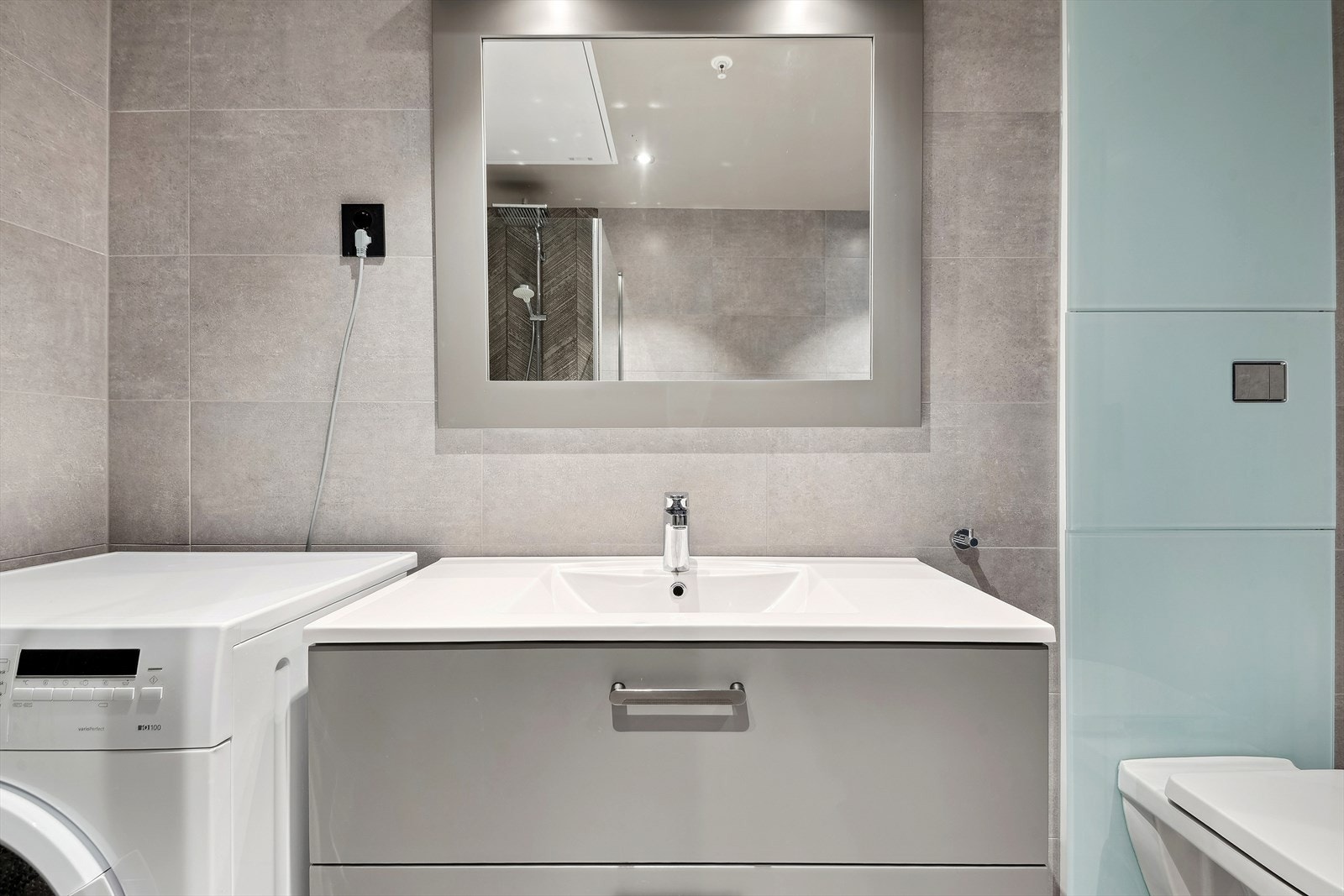 Servantinnredning, vegghengt toalett og dusjvegger i glass, samt opplegg for vaskemaskin. Galleribilde