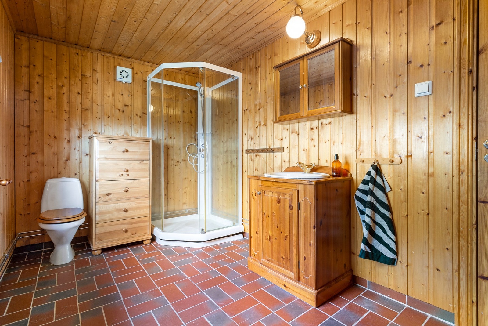 Baderom med toalett, servant med underskap og dusjkabinett. Flislagt gulv med varmekabler. Galleribilde