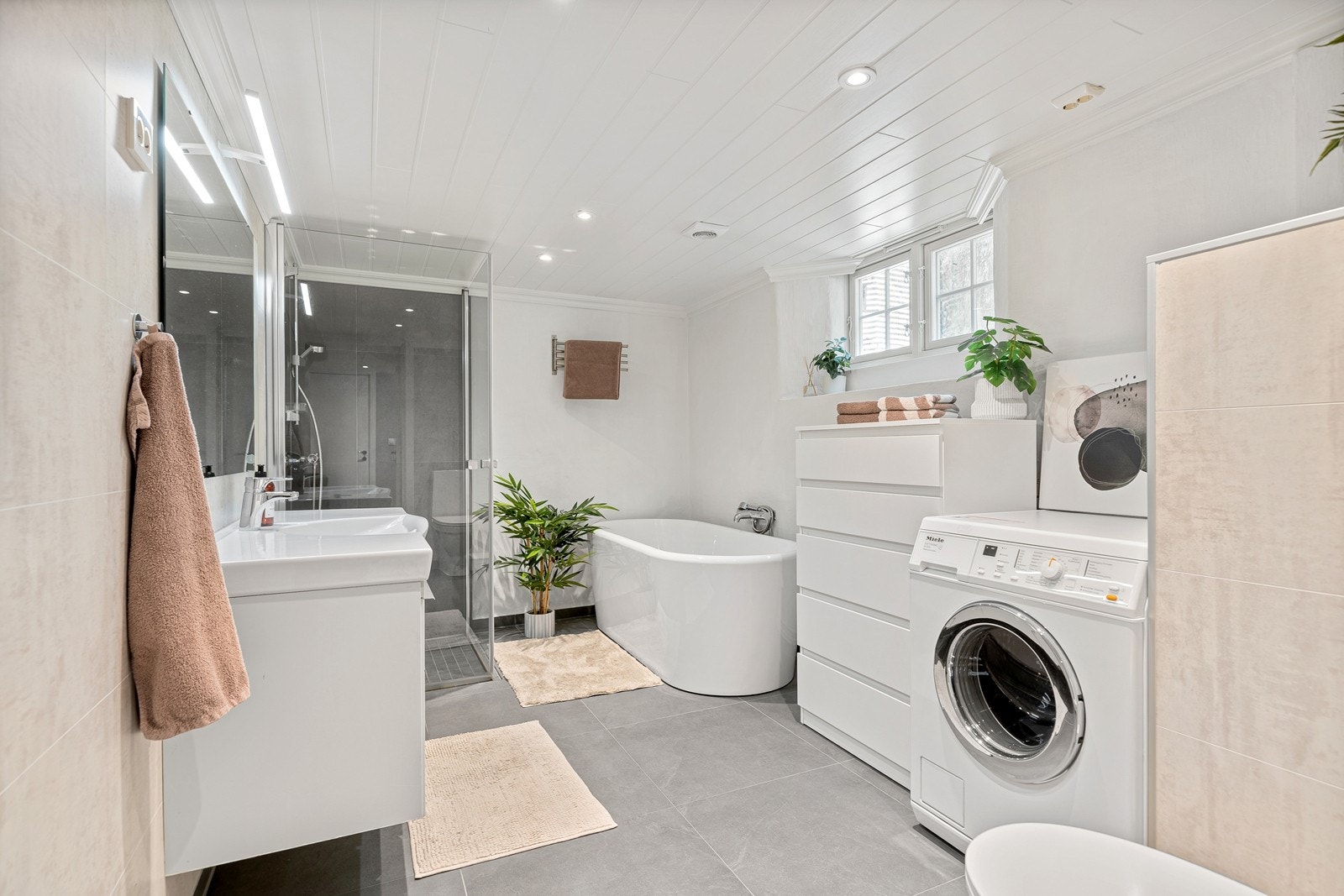 Badet er romslig og har både badekar og dusjnisje, stor servant med oppbevaring, vegghengt speil samt opplegg til vaskemaskin og tørketrommel. Galleribilde