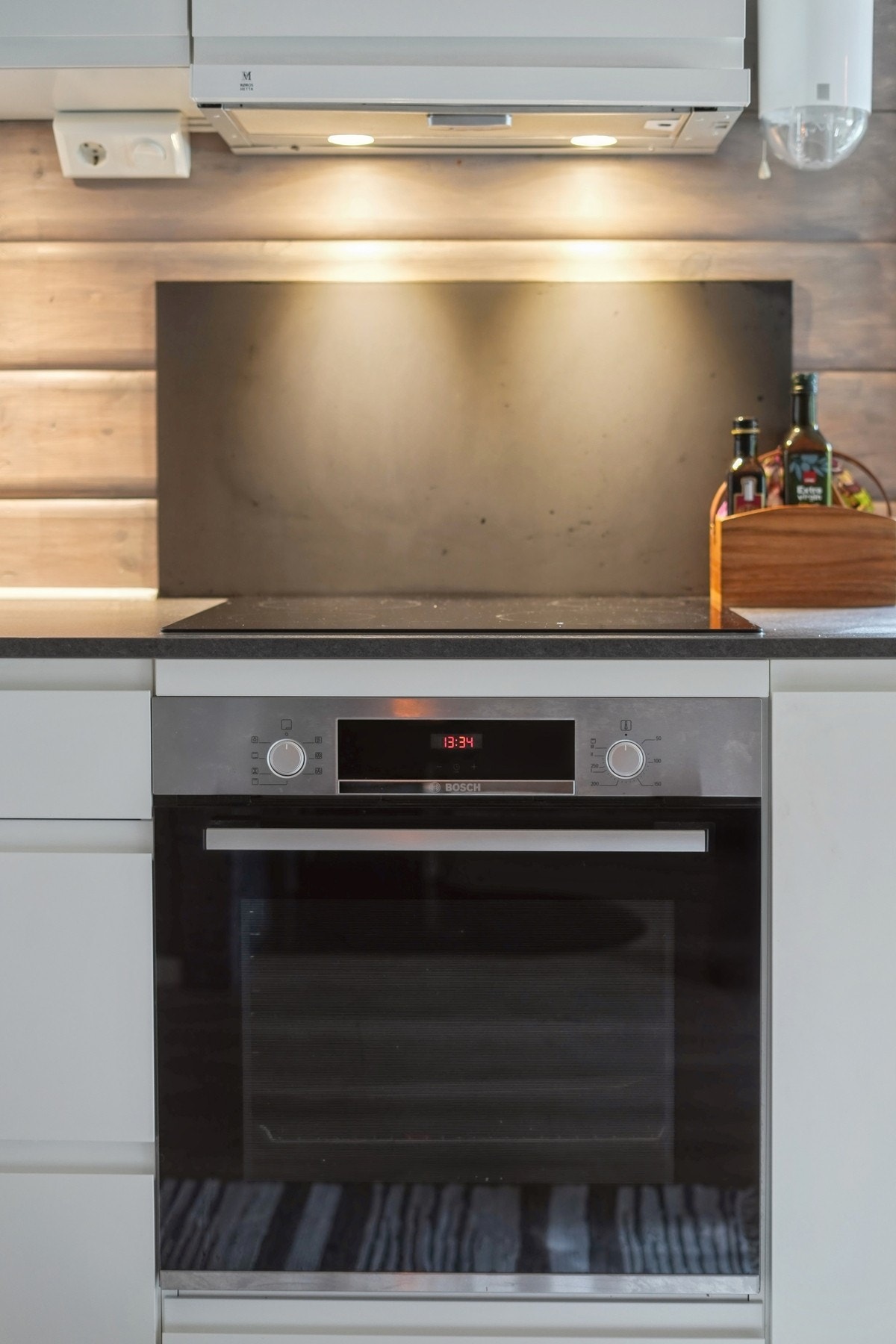 Kjøkkenventilator med avtrekk ut. Sort plate på vegg bak platetopp. Komfyrvakt montert. Galleribilde