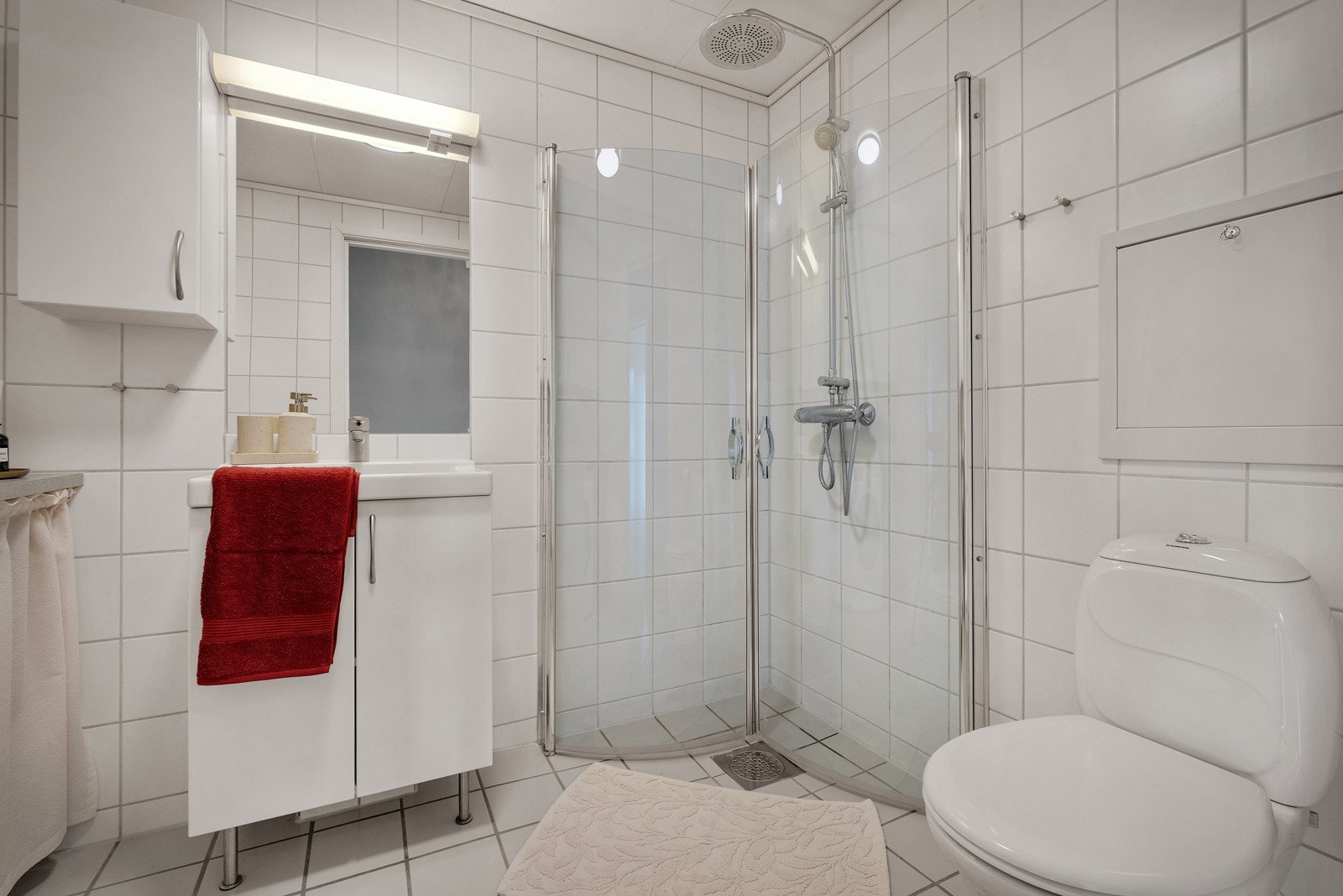 Det er innredet med dusjhjørne, toalett, og heldekkende servant med belysning over. Det er ellers innredet med overskap og benkeplate med vaskemaskin under. Galleribilde