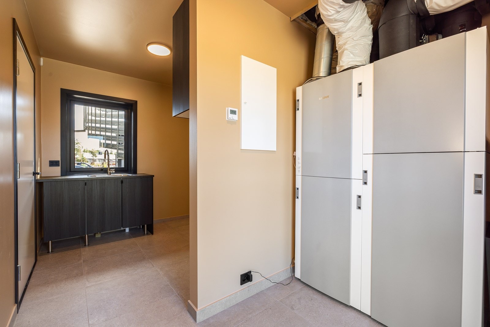 Praktisk vaskerom med flislagt gulv og malte, slette vegger. Galleribilde