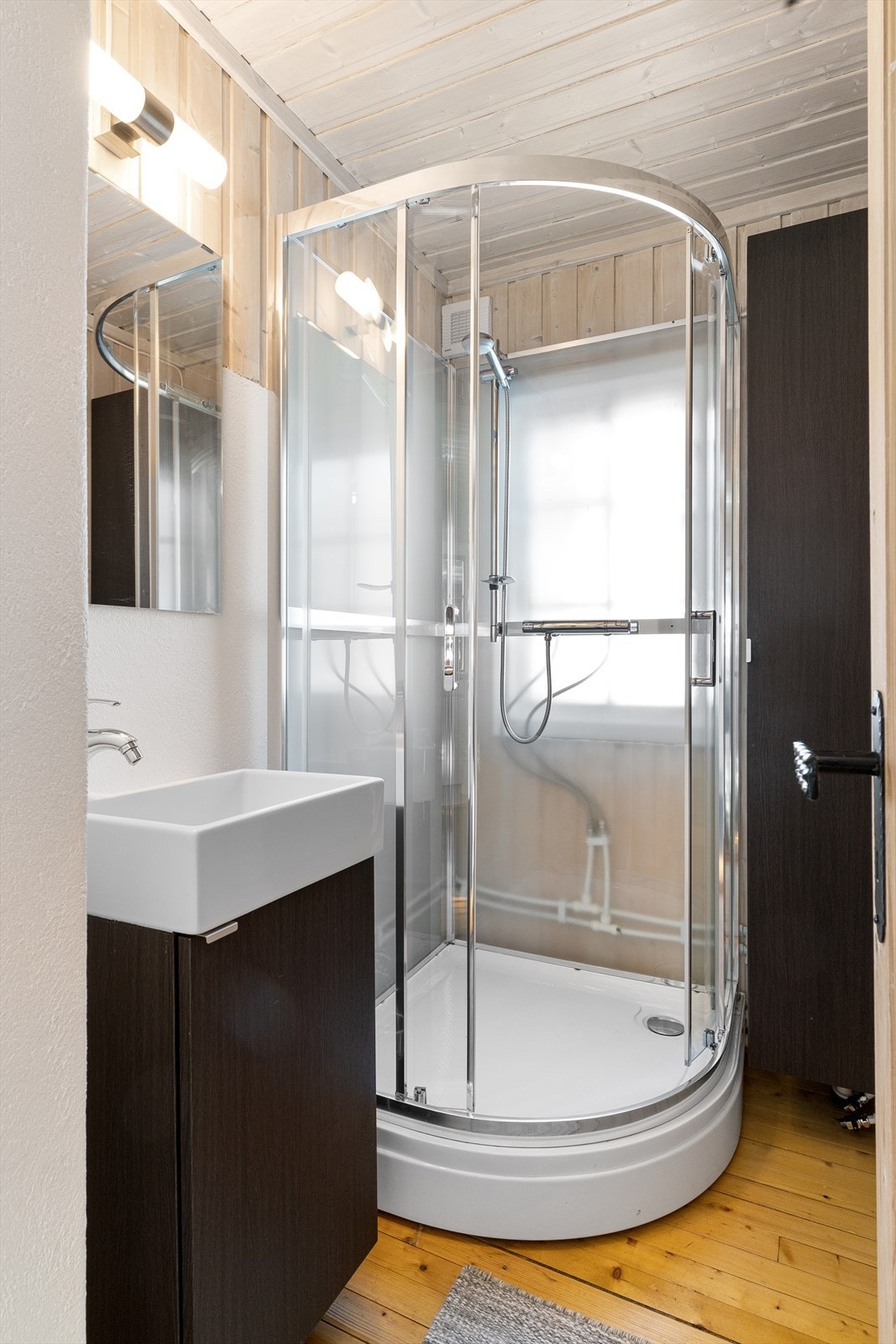 Hytten har eget bad med dusjkabinett og servant med underliggende skap. På rommet er det også satt inn et praktisk høyskap som gir god oppbevaringsplass. Galleribilde