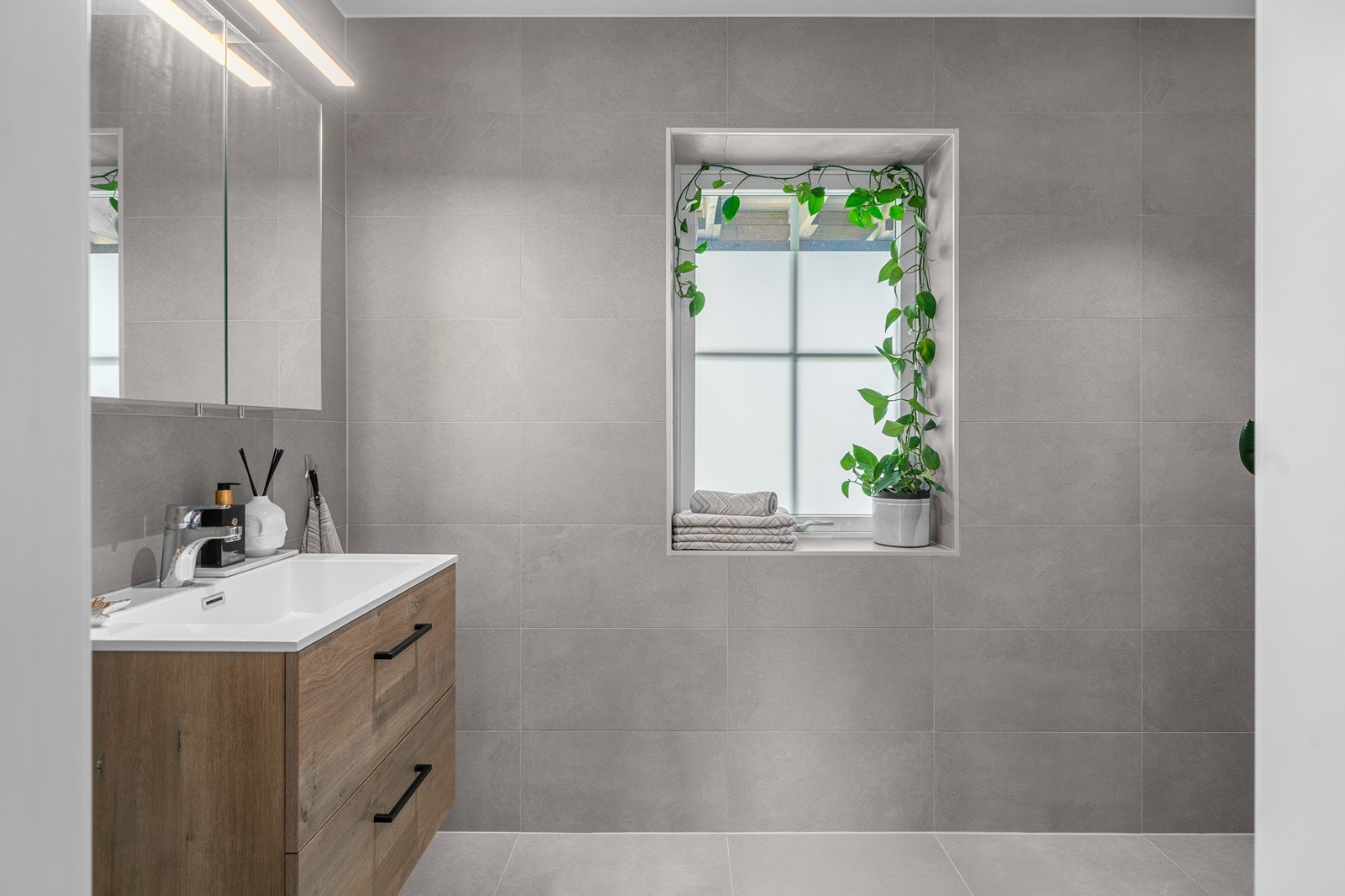 Boligen har et toalettrom med fliser på gulv og vegger, servantinnredning i naturfarge med skuffeseksjon og innebygd/vegghengt toalett. Galleribilde