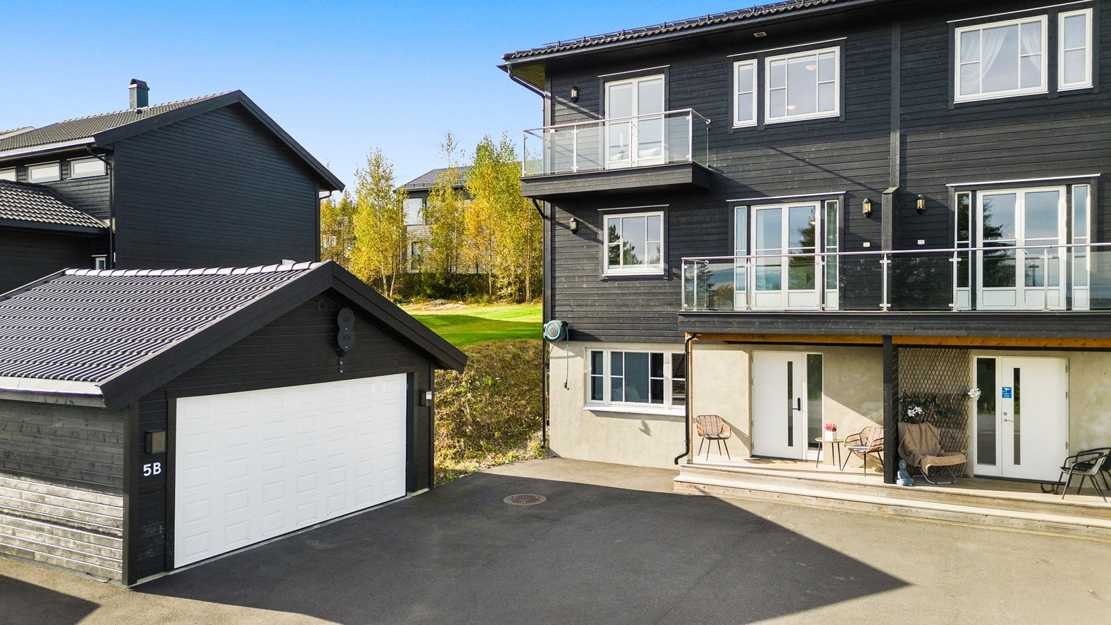 Skrånet tomt med asfaltert adkomstområde, opparbeidet gressplen på baksiden av tomannsboligen. Galleribilde