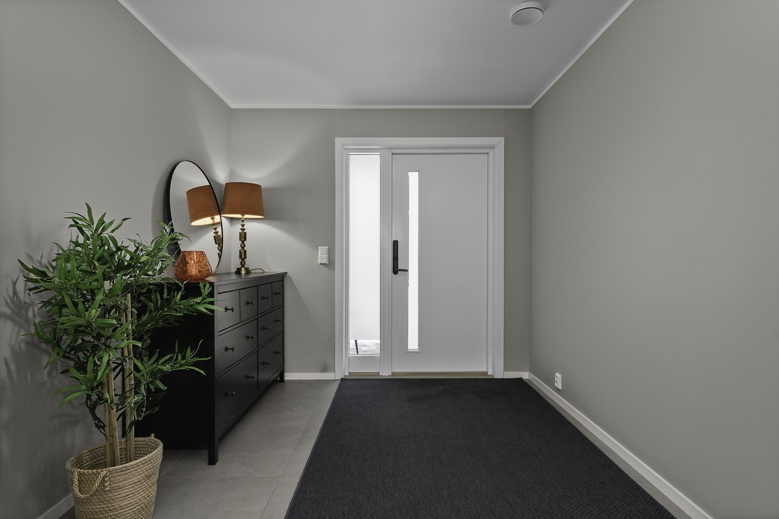 Et innbydende inngangsparti ønsker deg velkommen- innenfor døren blir man møtt av boligens entrè som har fliser på gulvet og gråmalte vegger. Det er god plass til skohylle og skap for oppheng av yttertøy. Galleribilde