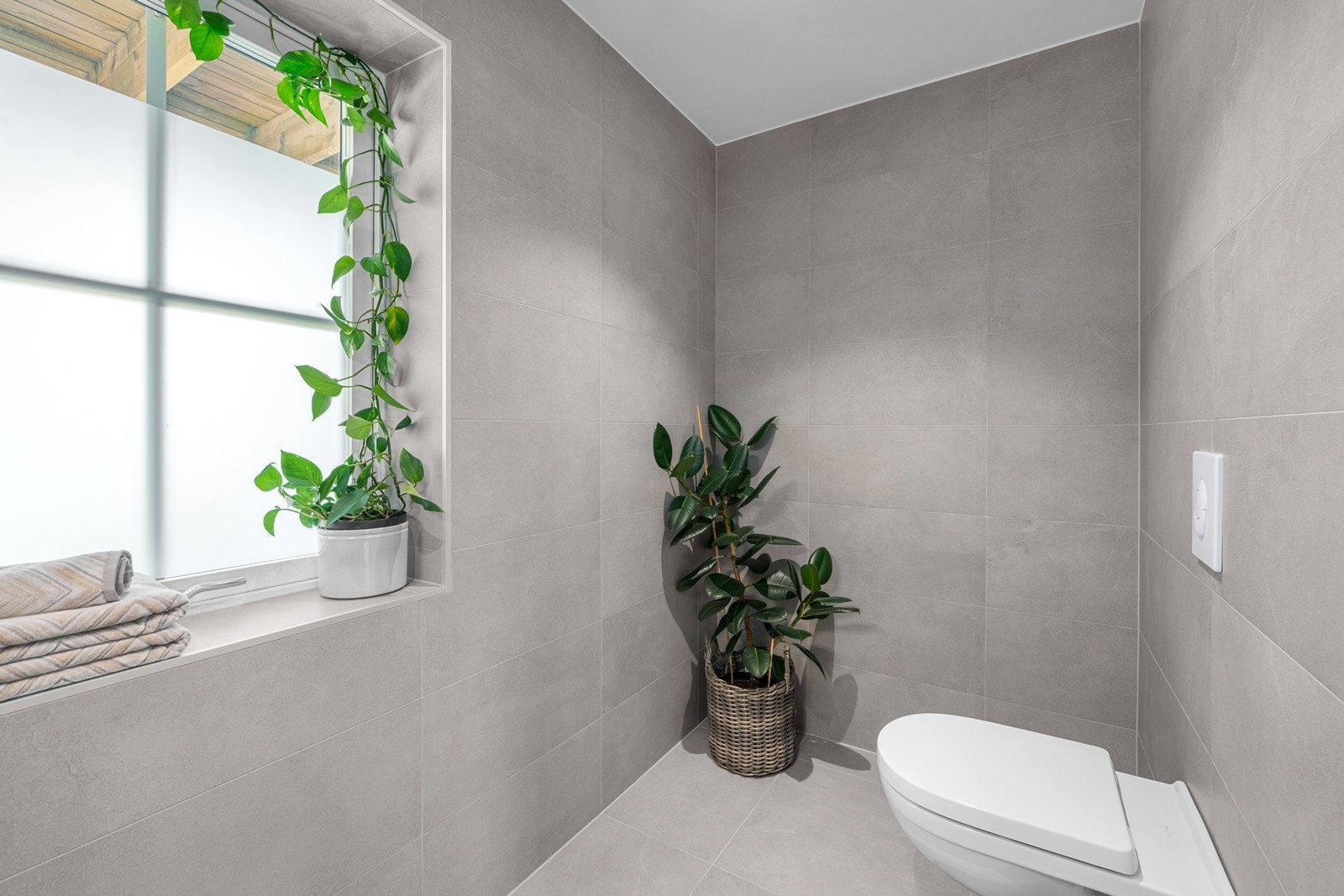 Boligen har et toalettrom med fliser på gulv og vegger, servantinnredning i naturfarge med skuffeseksjon og innebygd/vegghengt toalett. Galleribilde