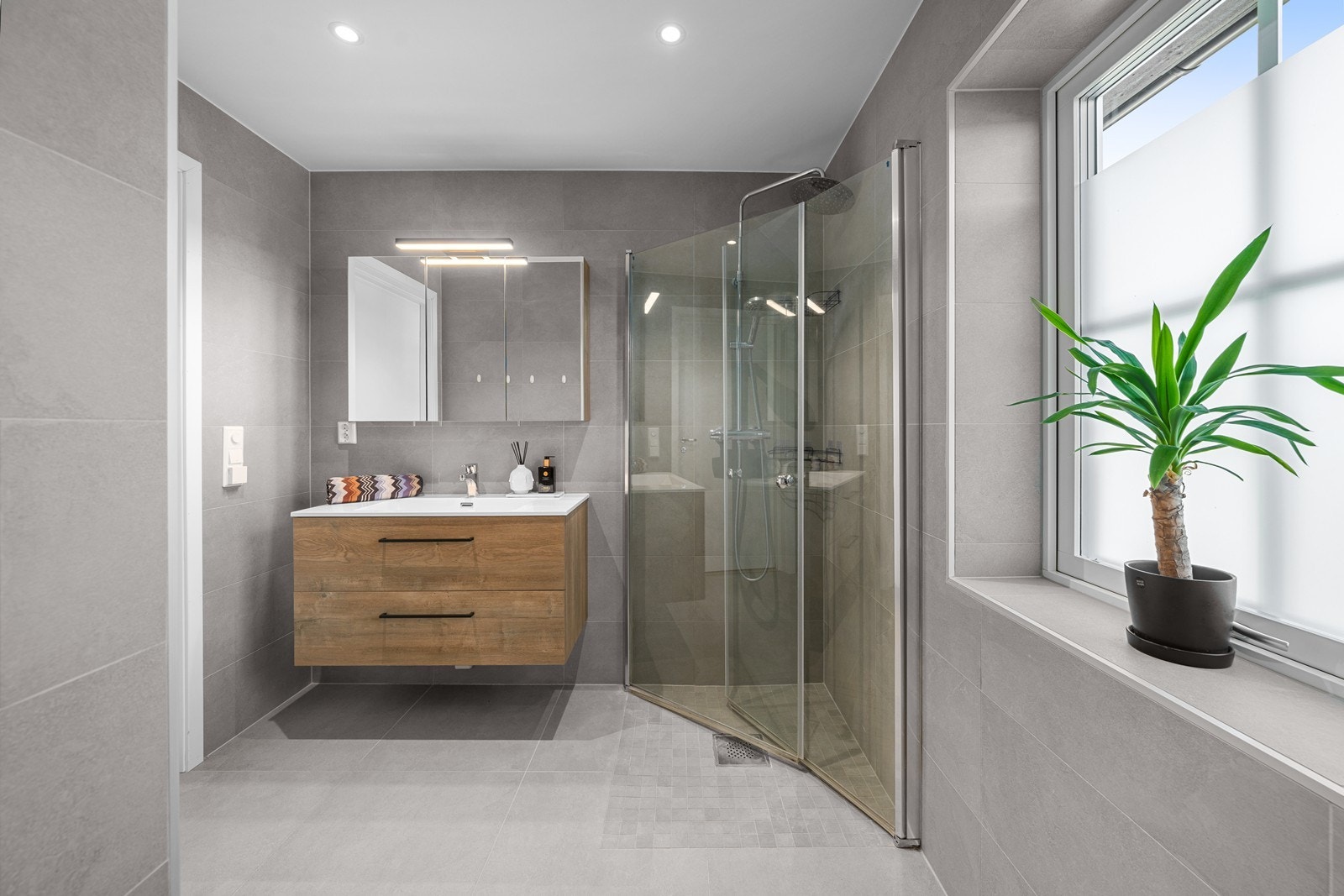 Det andre baderommet har fliser på gulv og vegger, sort servantinnredning med skuffeseksjon, dusjnisje med regnfallsdusj og skyvedør av glass og innebygd/vegghengt toalett. Galleribilde