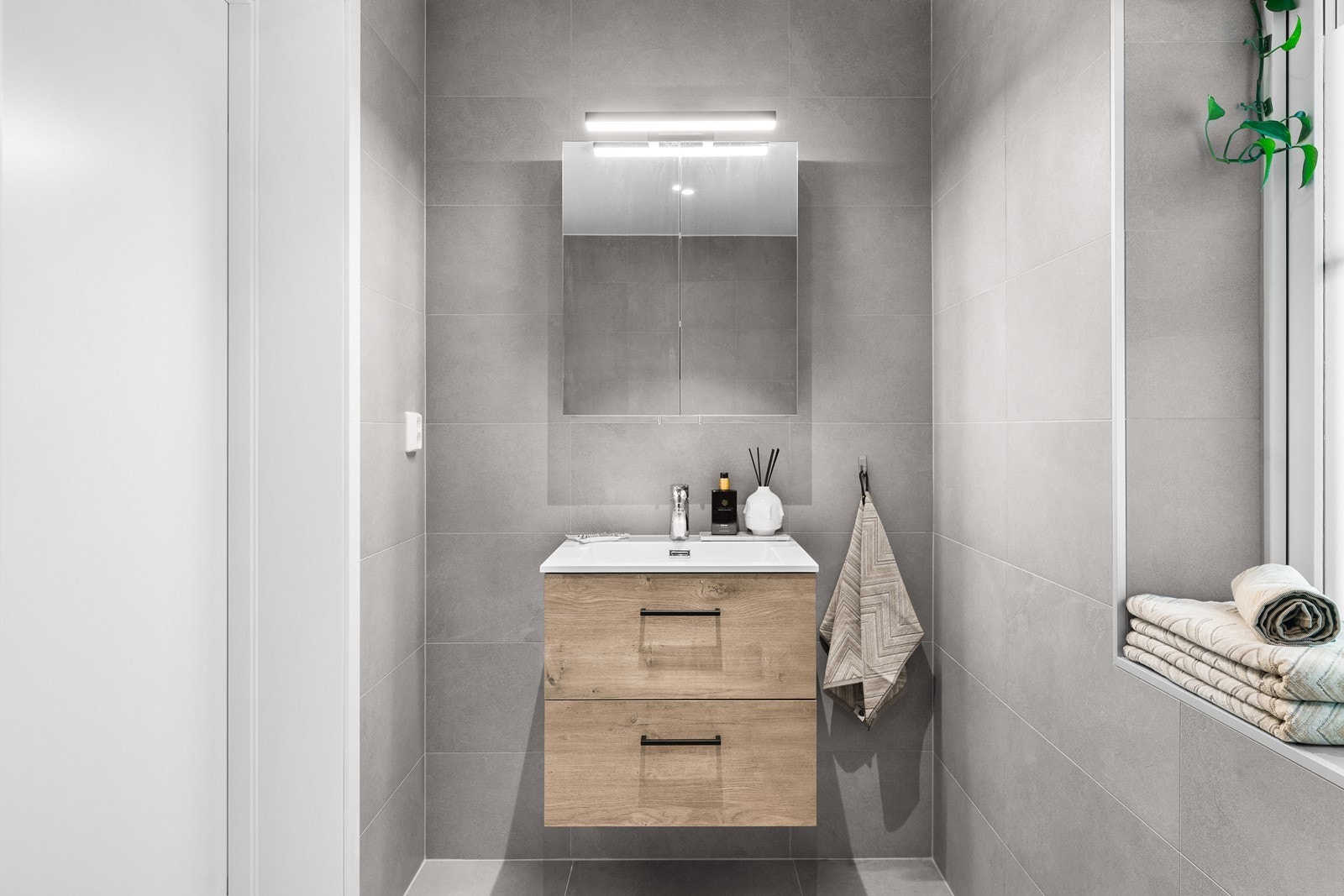 Boligen har et toalettrom med fliser på gulv og vegger, servantinnredning i naturfarge med skuffeseksjon og innebygd/vegghengt toalett. Galleribilde