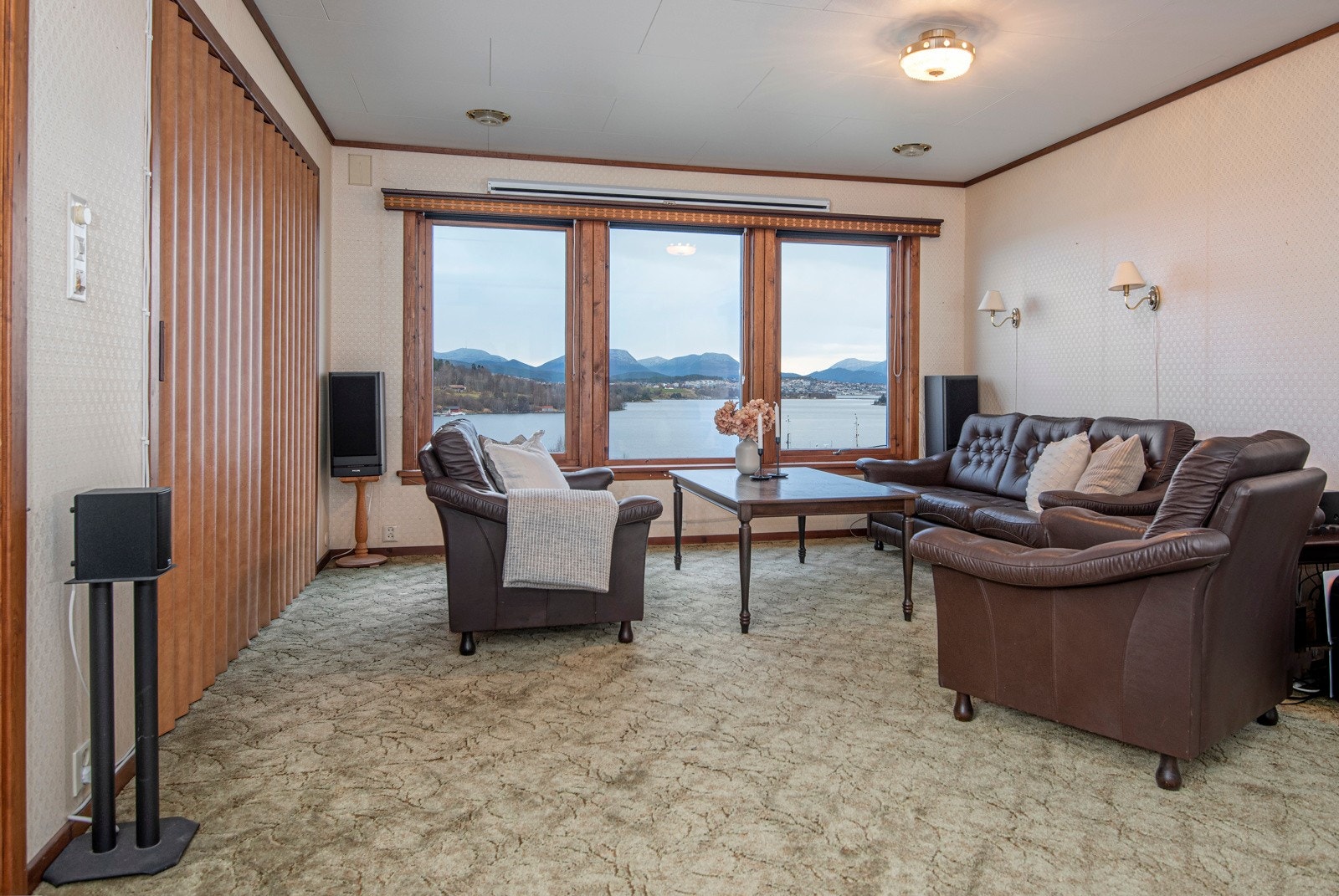 Stuen i 1.etasje har tepper på gulvet og tapet på veggene. Det er trekkspilldører inn til TV-stue. Galleribilde